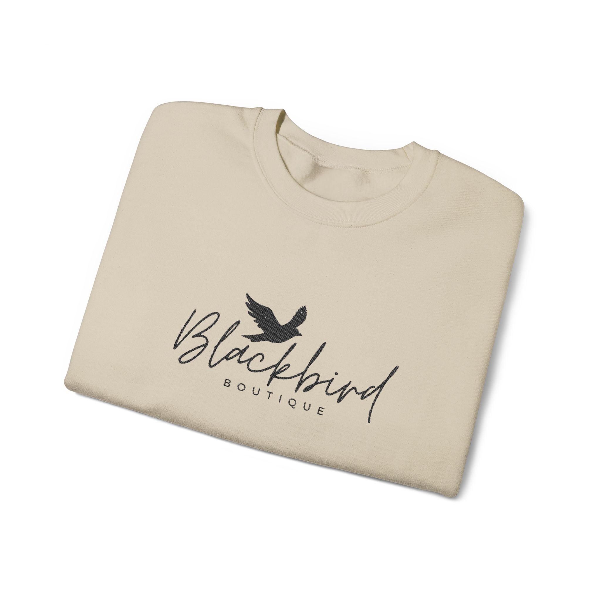 A folded cream-colored t-shirt with a black graphic print of a bird and the text 'Blackbird BOUTIQUE' on the front, displayed on a clean white background.