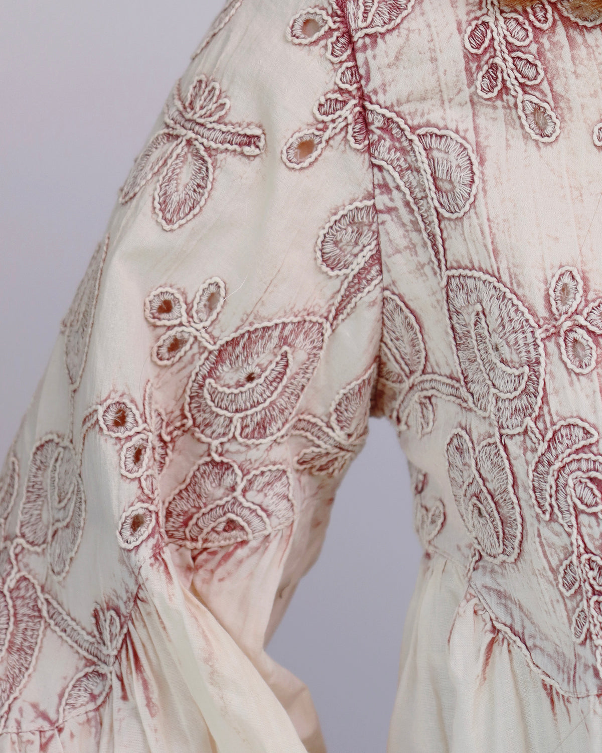 Close-up of a cream-colored fabric garment with intricate dusty rose embroidery and floral detailing.