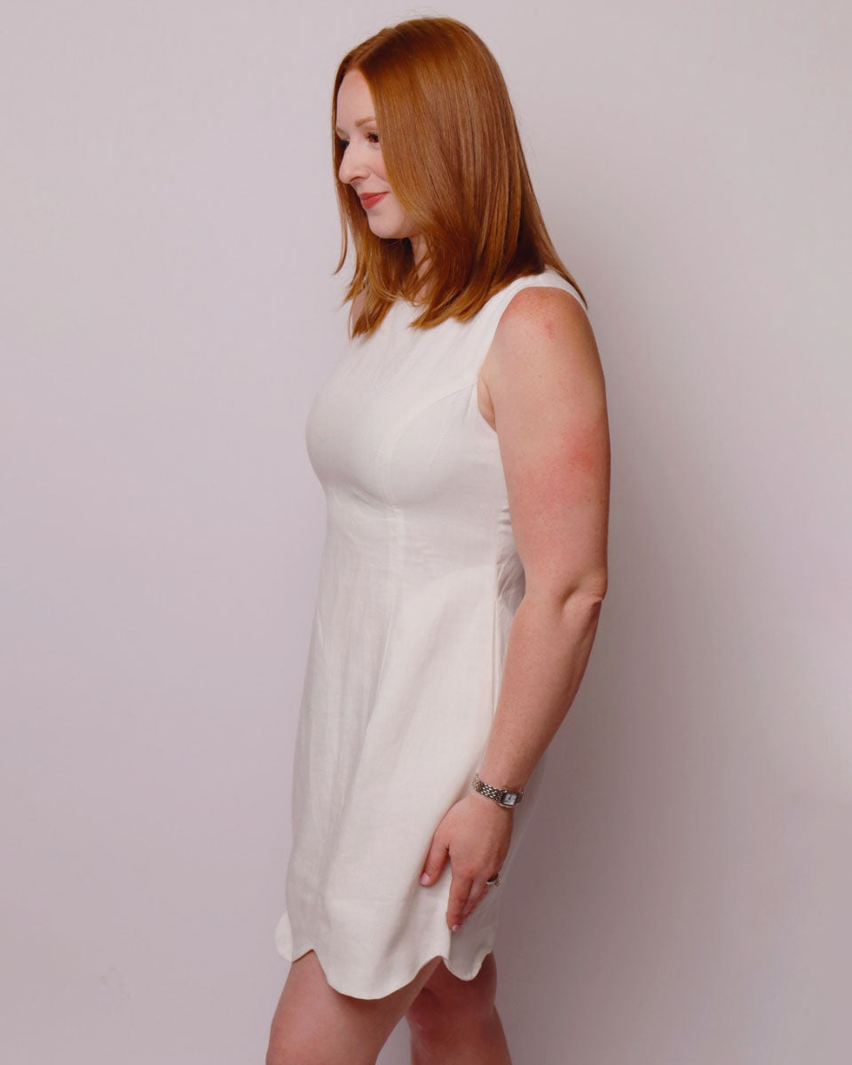 Woman wearing a white sleeveless dress against a plain background