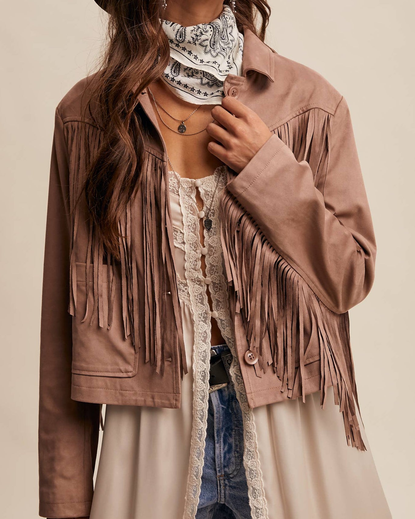 Woman wearing a brown fringed jacket, hat, and scarf against a beige background