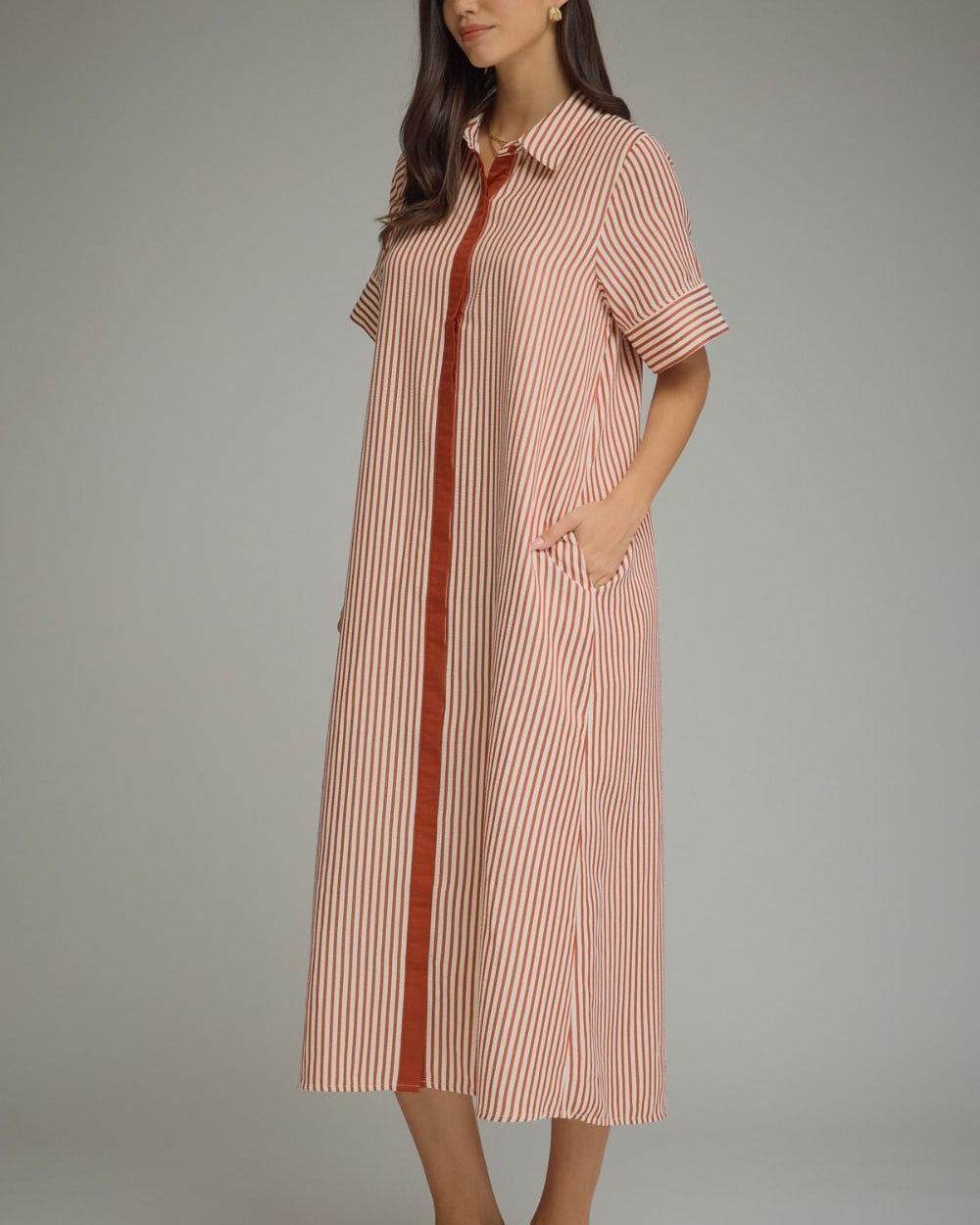 Woman wearing a long striped dress with a red accent on a gray background