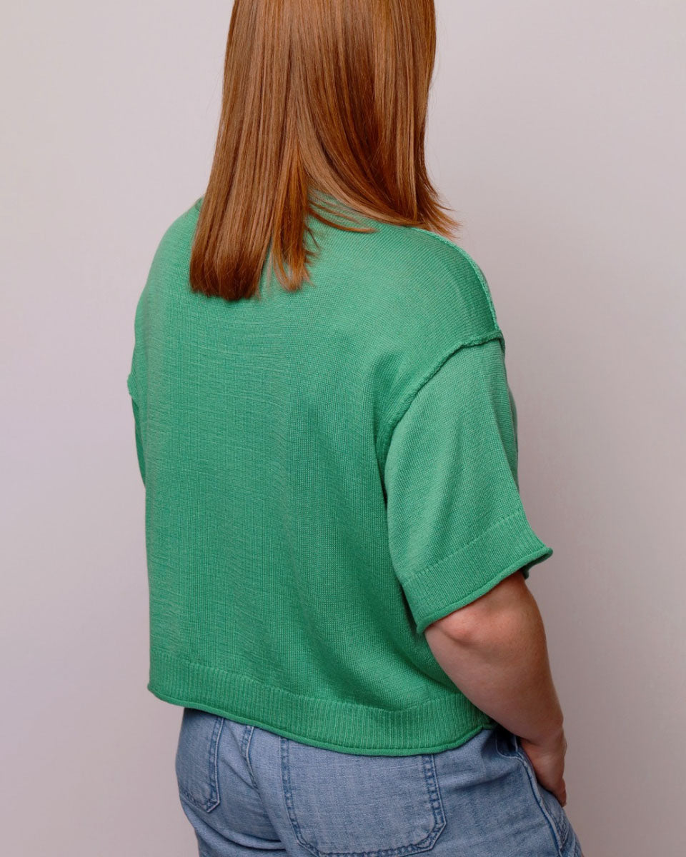 Person wearing a green sweater and blue jeans against a plain background