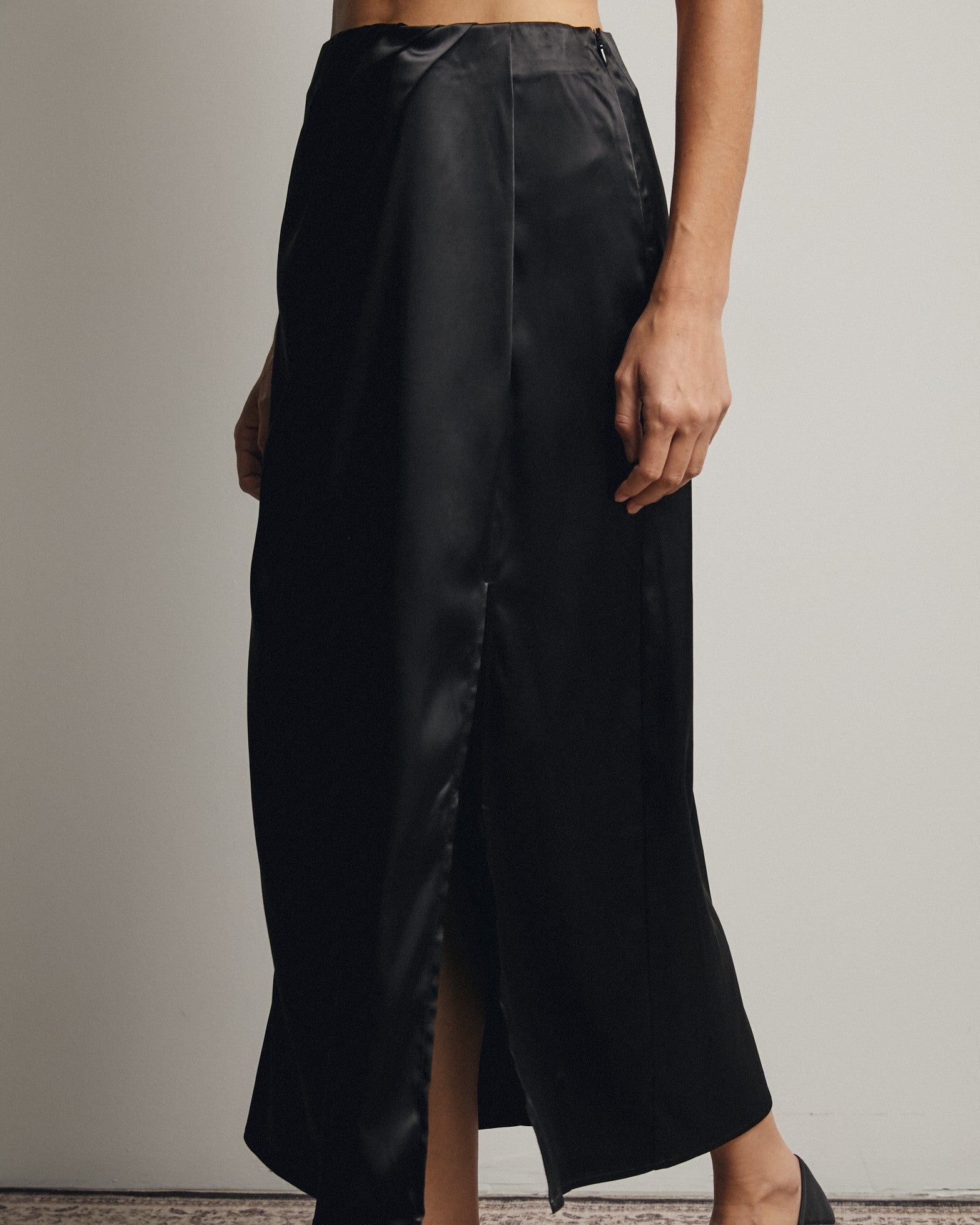 Person wearing a black satin skirt with a plain background