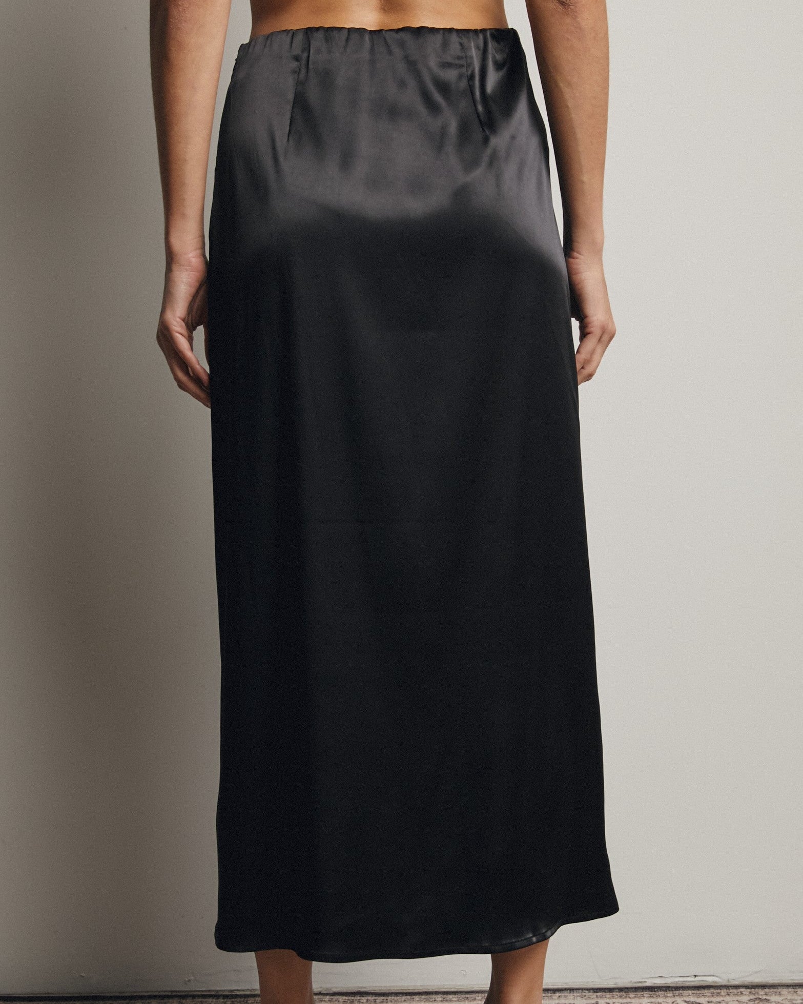 Person wearing a black satin skirt against a neutral background