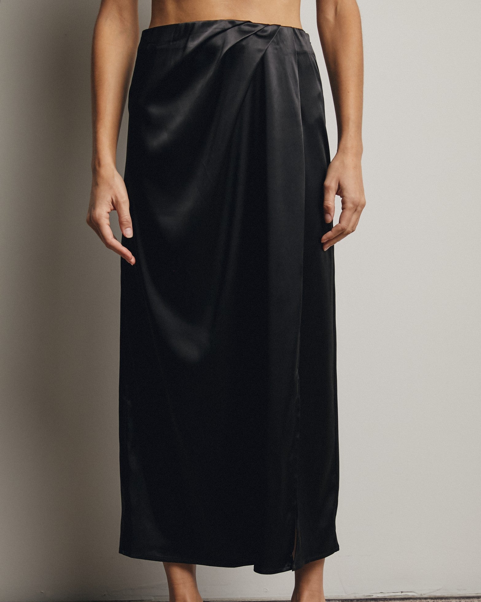 Person wearing a black satin skirt against a neutral background