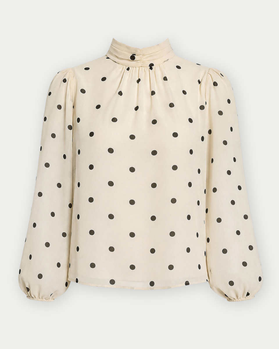 A cream-colored long-sleeve blouse with black polka dots, featuring a high gathered mock neck and puffed balloon sleeves, shown against a light gray background.