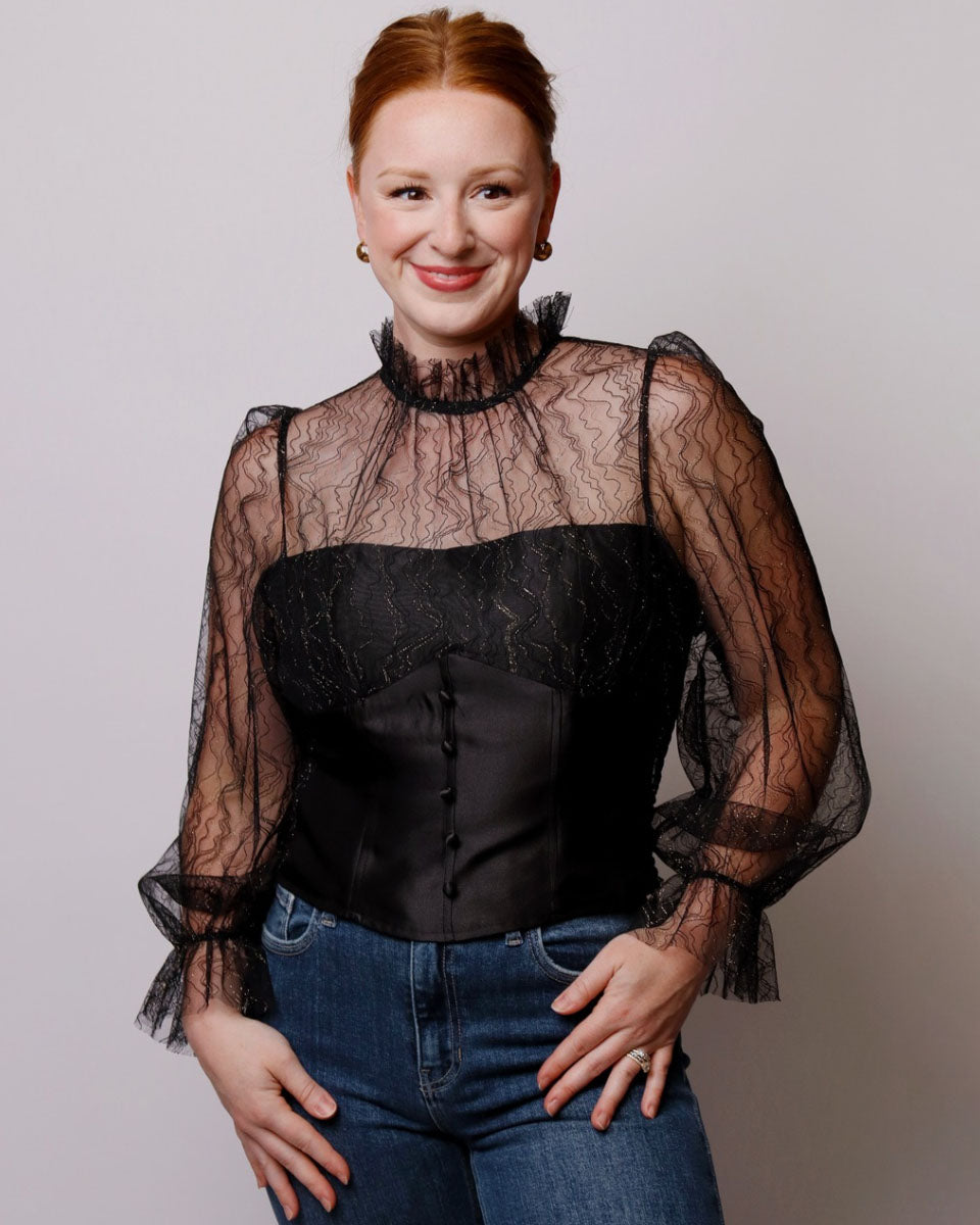 Woman wearing a black lace top and jeans against a plain background