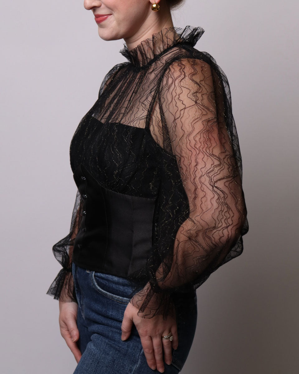 Person wearing a black lace top with sheer sleeves against a plain background