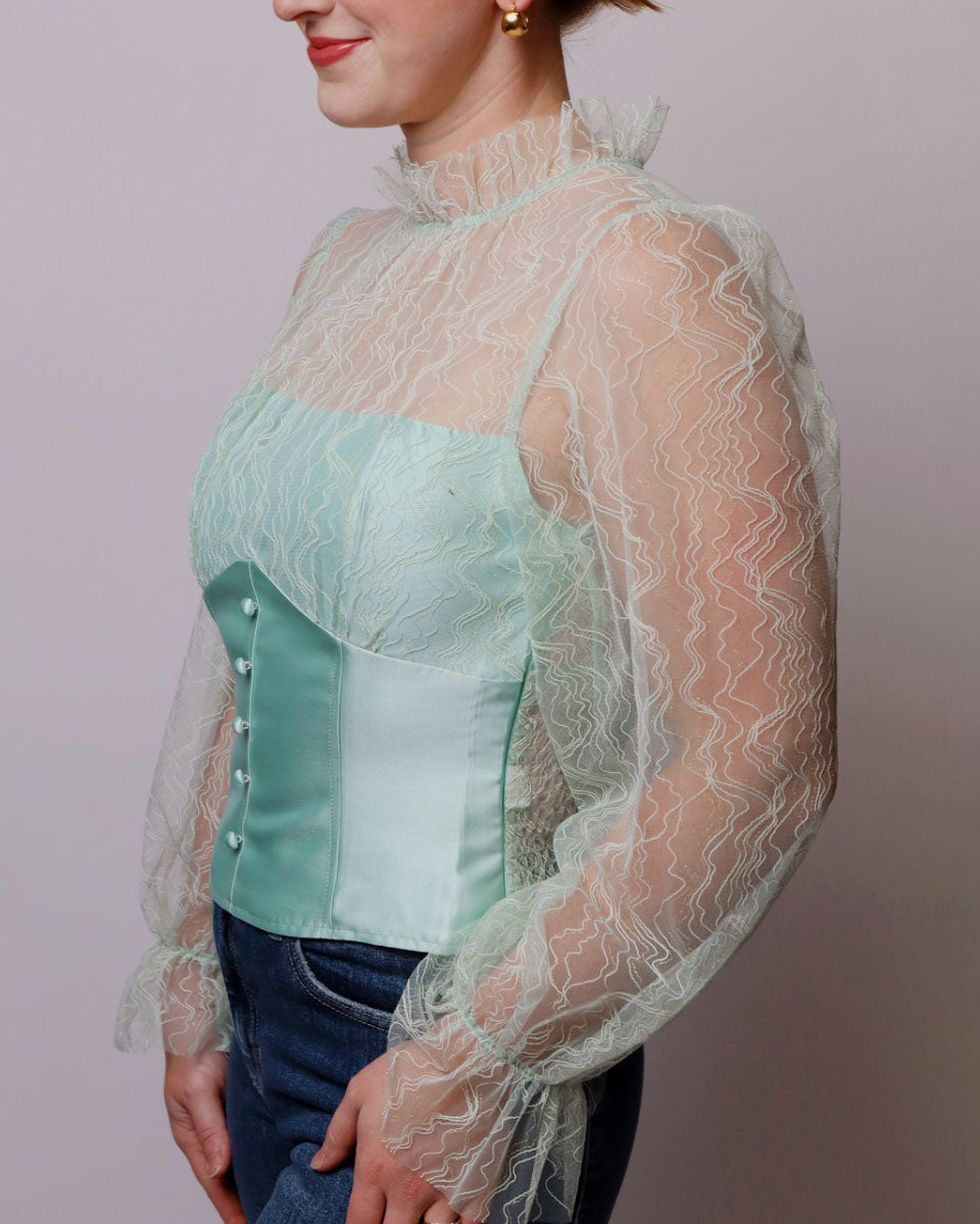 Person wearing a light green blouse with sheer sleeves against a plain background