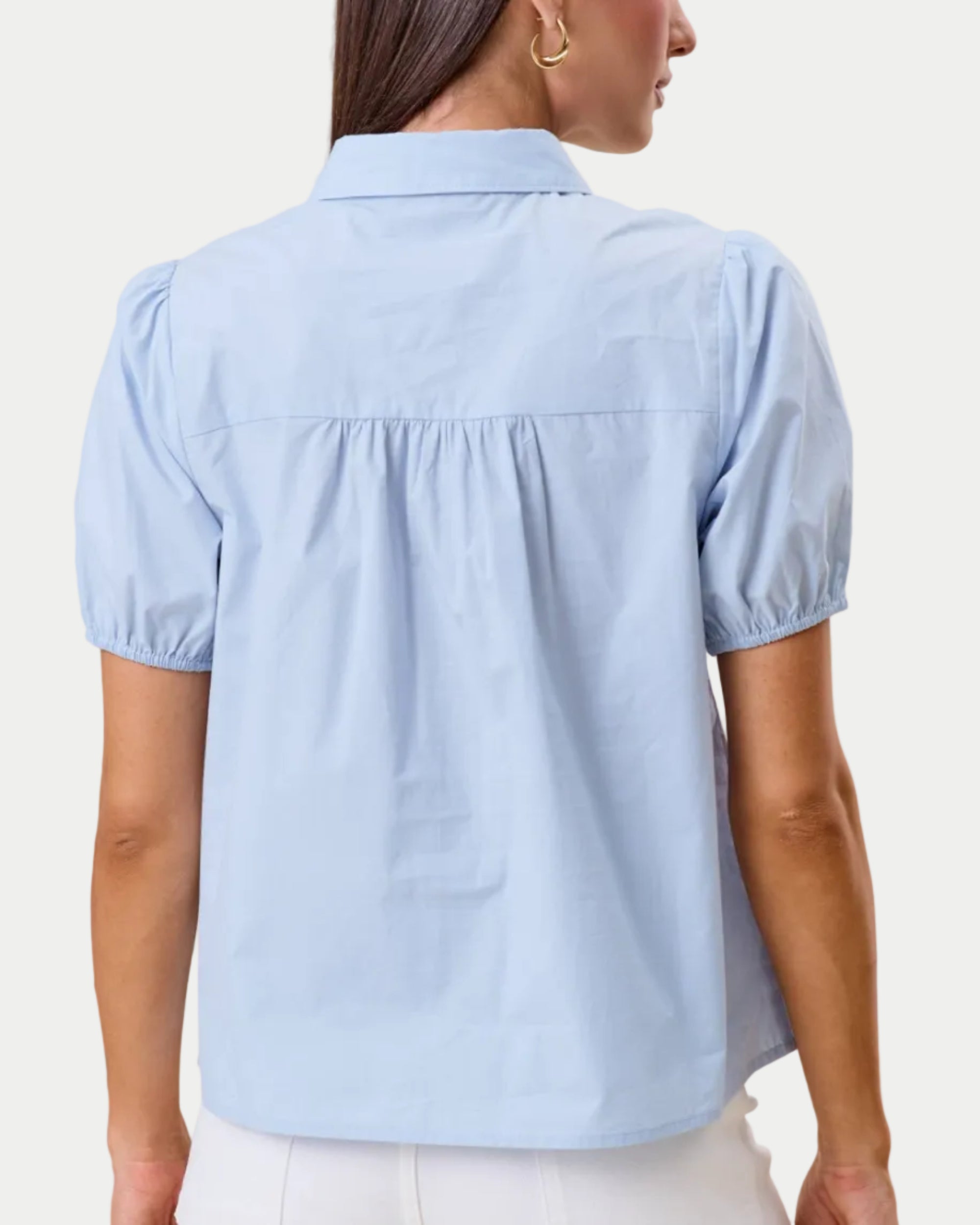 Cutwork blouse. Sky blue on a model with a neutral background. Cutout detail around the neckline. back view