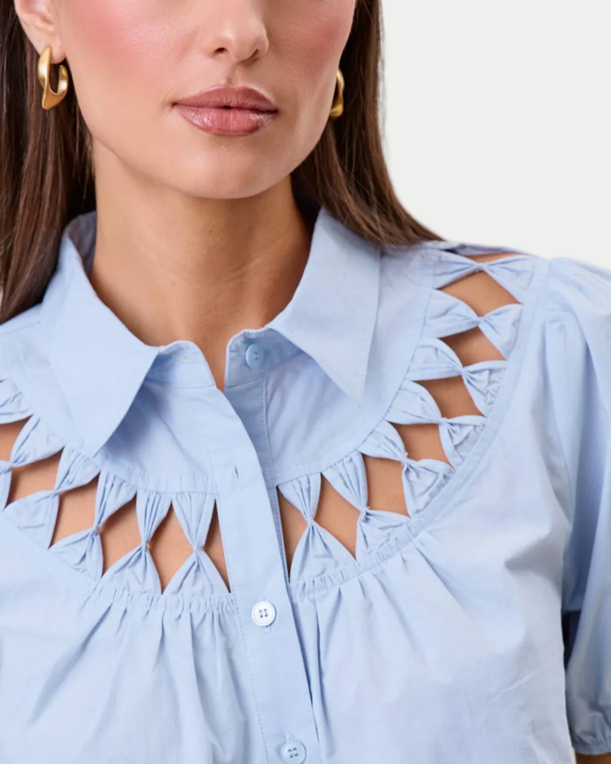 Cutwork blouse. Sky blue on a model with a neutral background. Cutout detail around the neckine. closeup of neckline