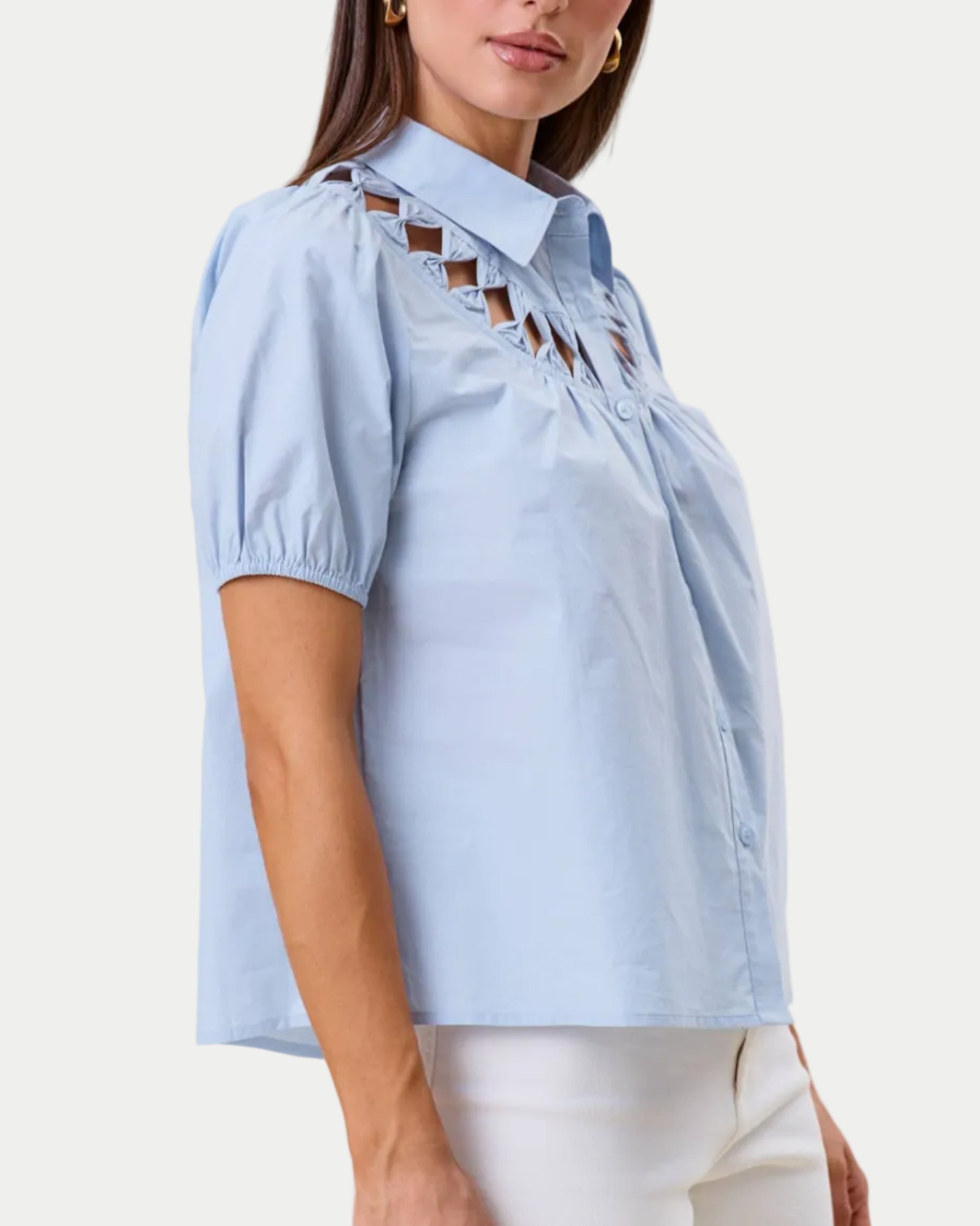 Cutwork blouse. Sky blue on a model with a neutral background. Cutout detail around the neckline. Side view