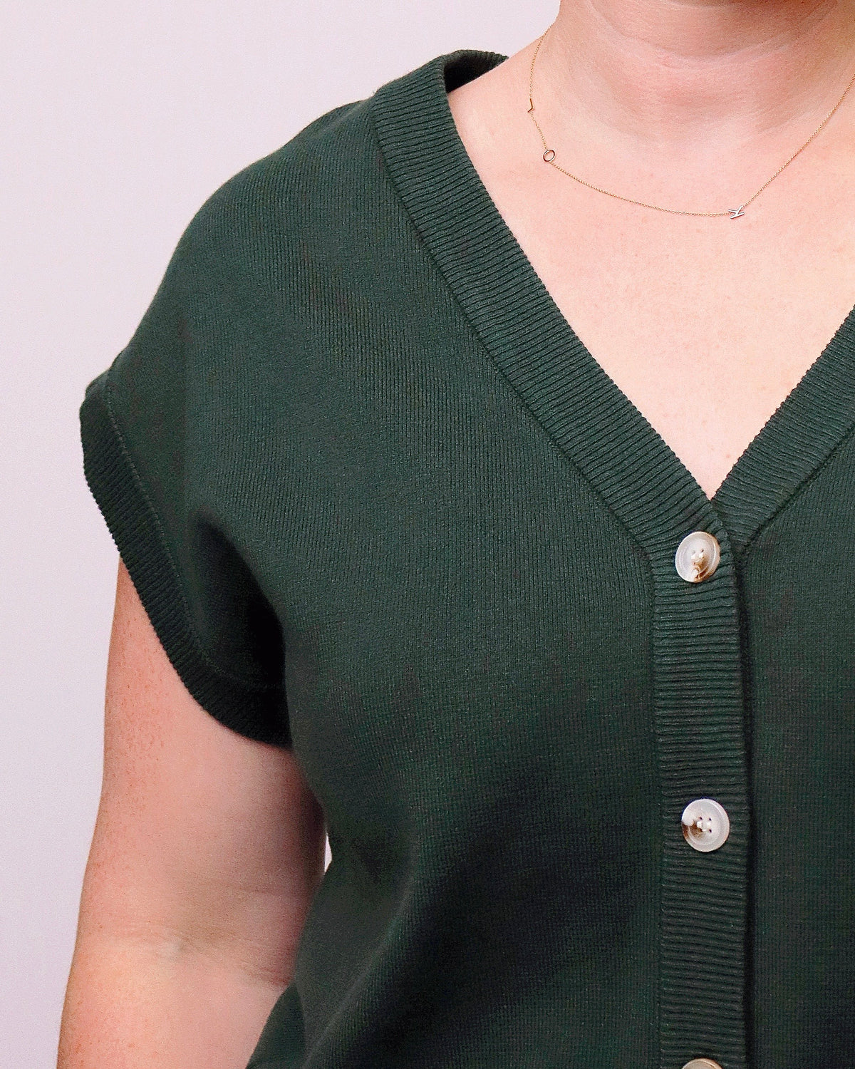 Close-up of a person wearing a dark forest green short-sleeve knit cardigan with a ribbed V-neck and front buttons.