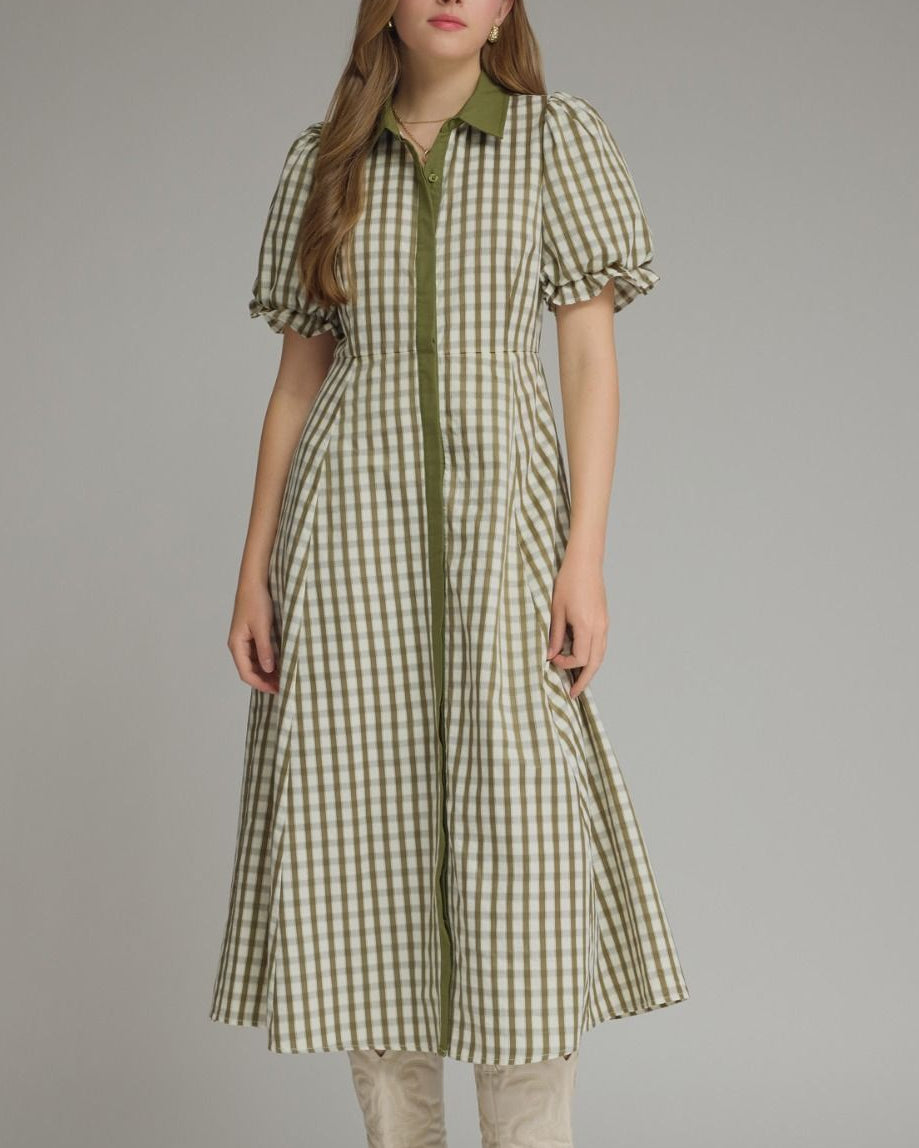 Woman wearing a green and white checkered dress with beige boots on a gray background
