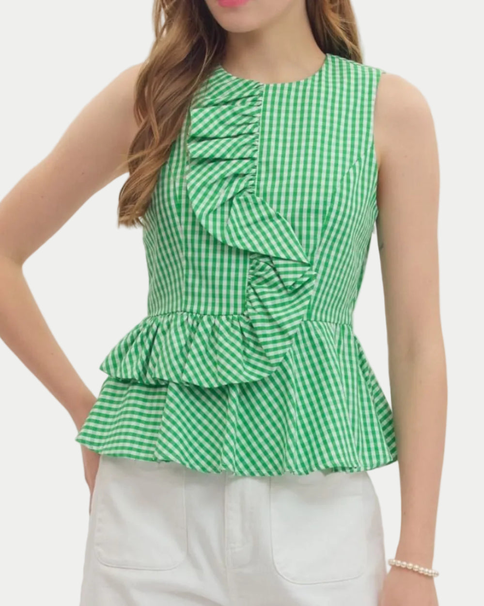 Woman wearing a green checkered peplum top and white shorts on a plain background. unique sleeveles top. Summer top. Vacation Top. Weekend wear.