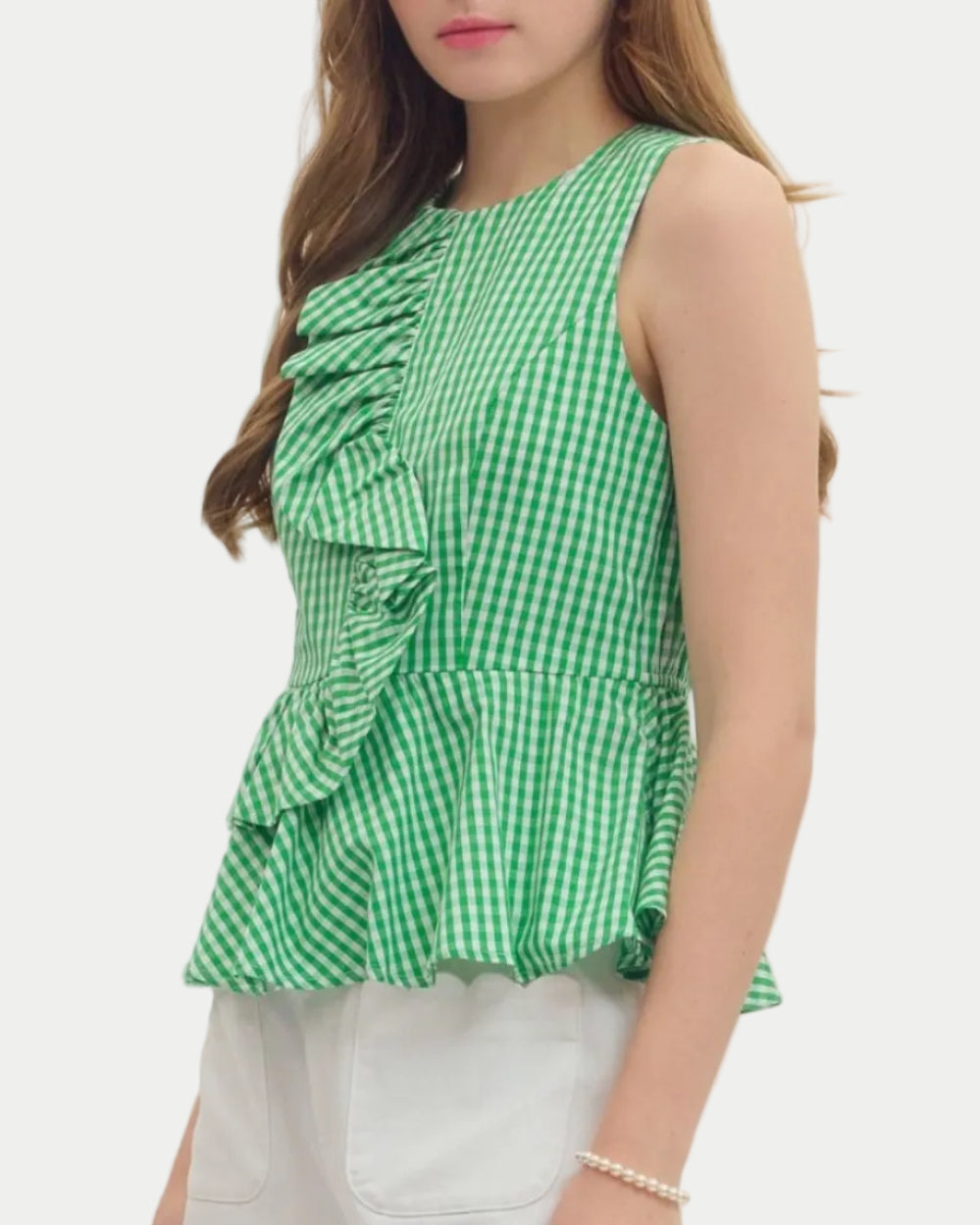 Woman wearing a green checkered peplum top and white shorts on a plain background. unique sleeveles top. Summer top. Vacation Top. Weekend wear.
