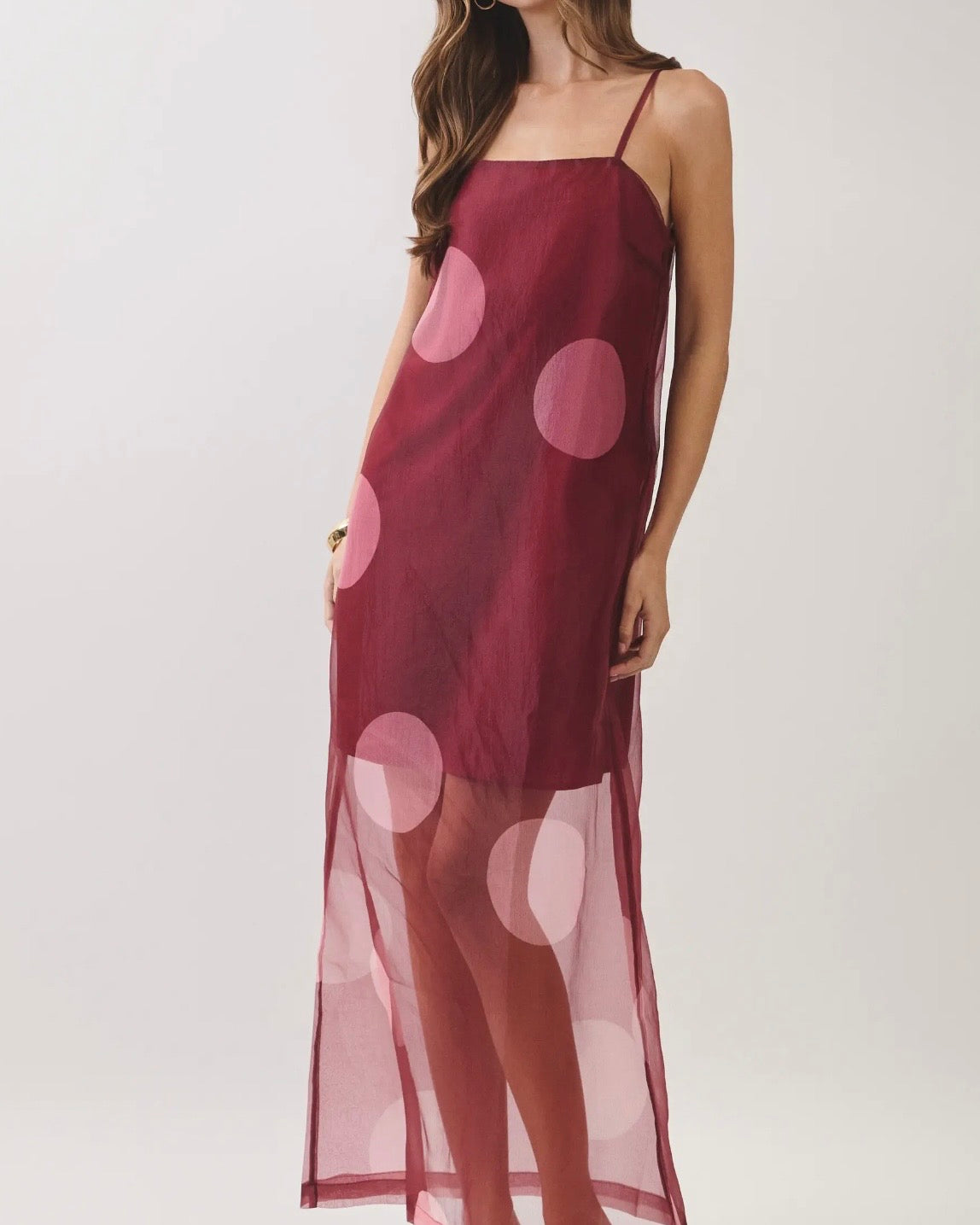Model wearing a burgundy dress with a sheer overlay with large polkadots on a neutral background