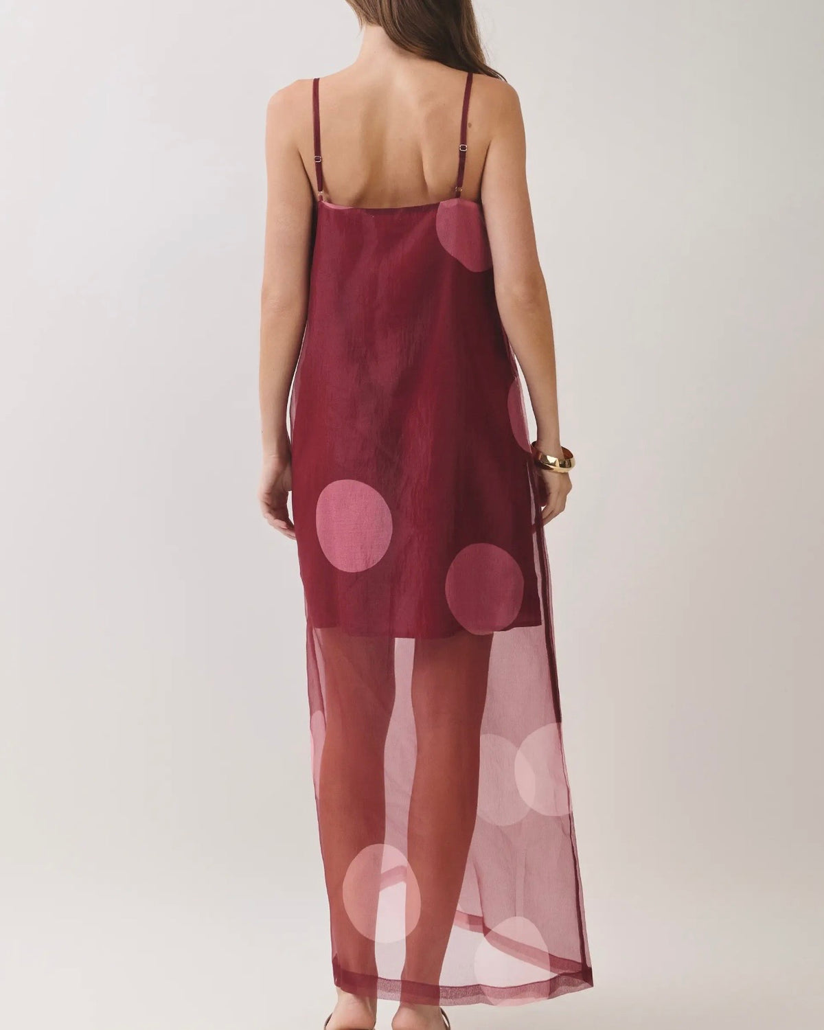 Model wearing a burgundy dress with a sheer overlay with large polkadots on a neutral background