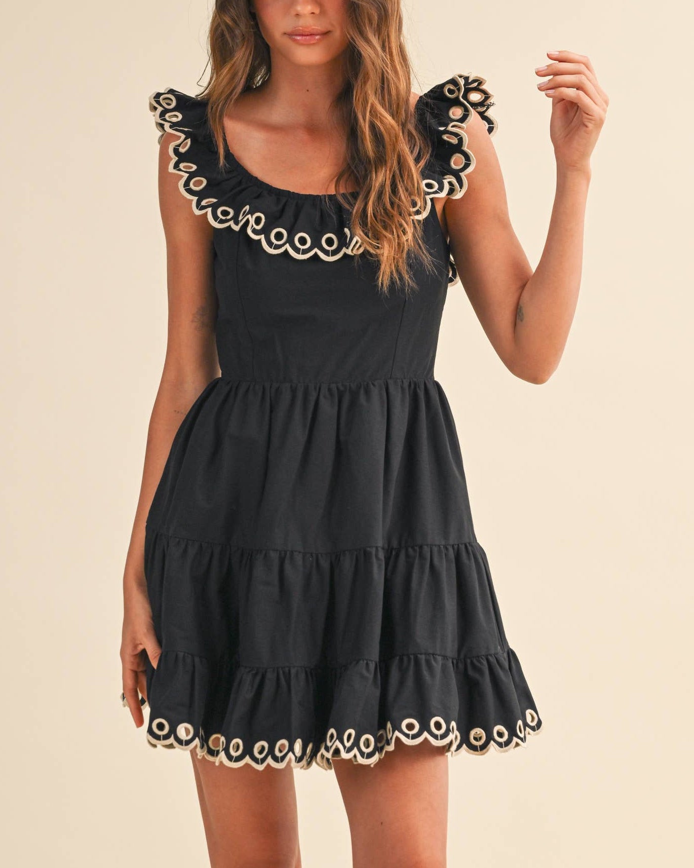 Woman wearing a black dress with white embroidery on a beige background