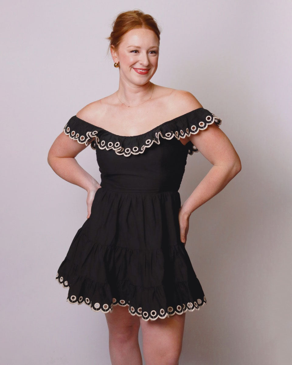 Woman wearing a black off-shoulder dress with white trim against a plain background