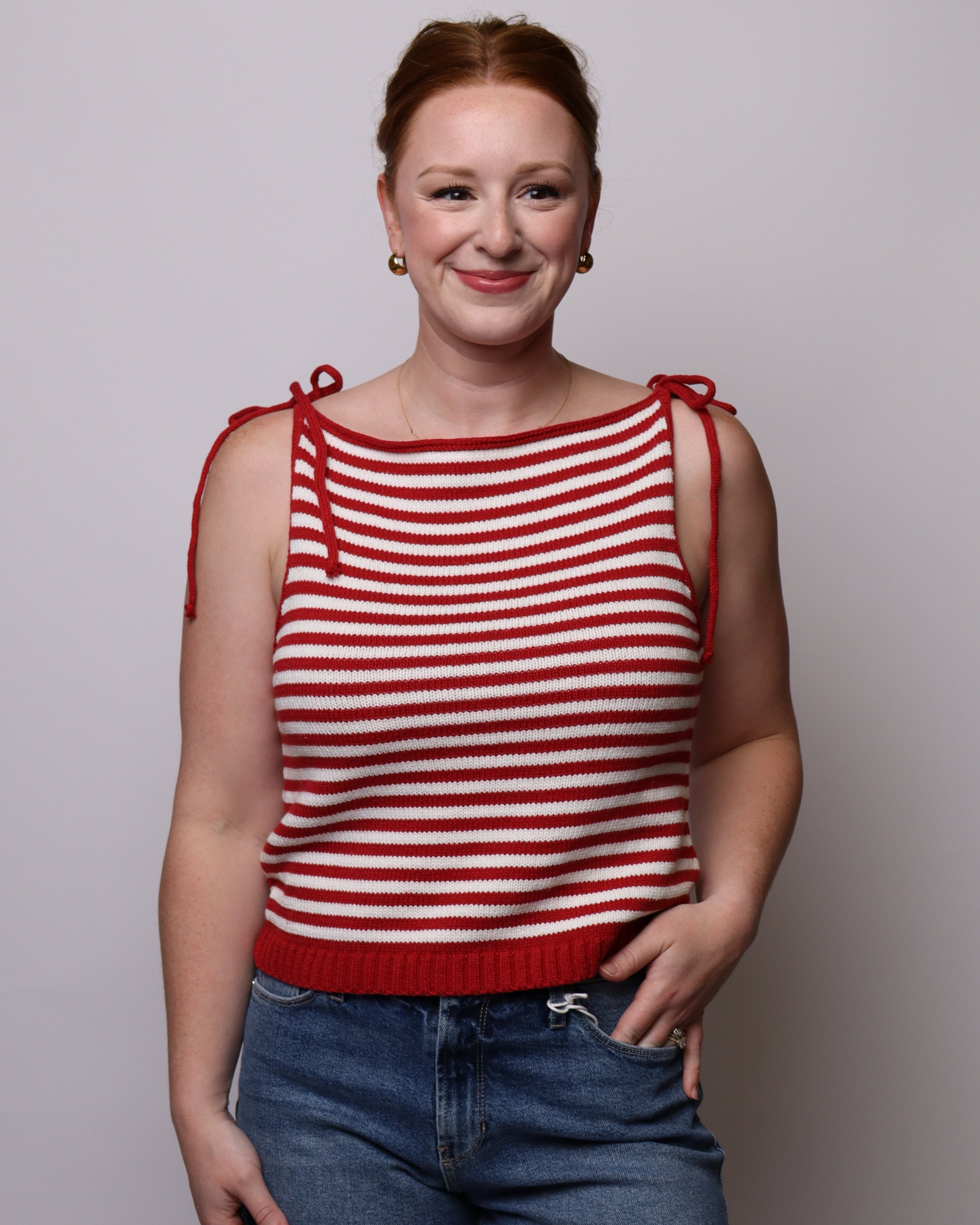 Person wearing a red and white striped tank top and denim shorts on a plain background
