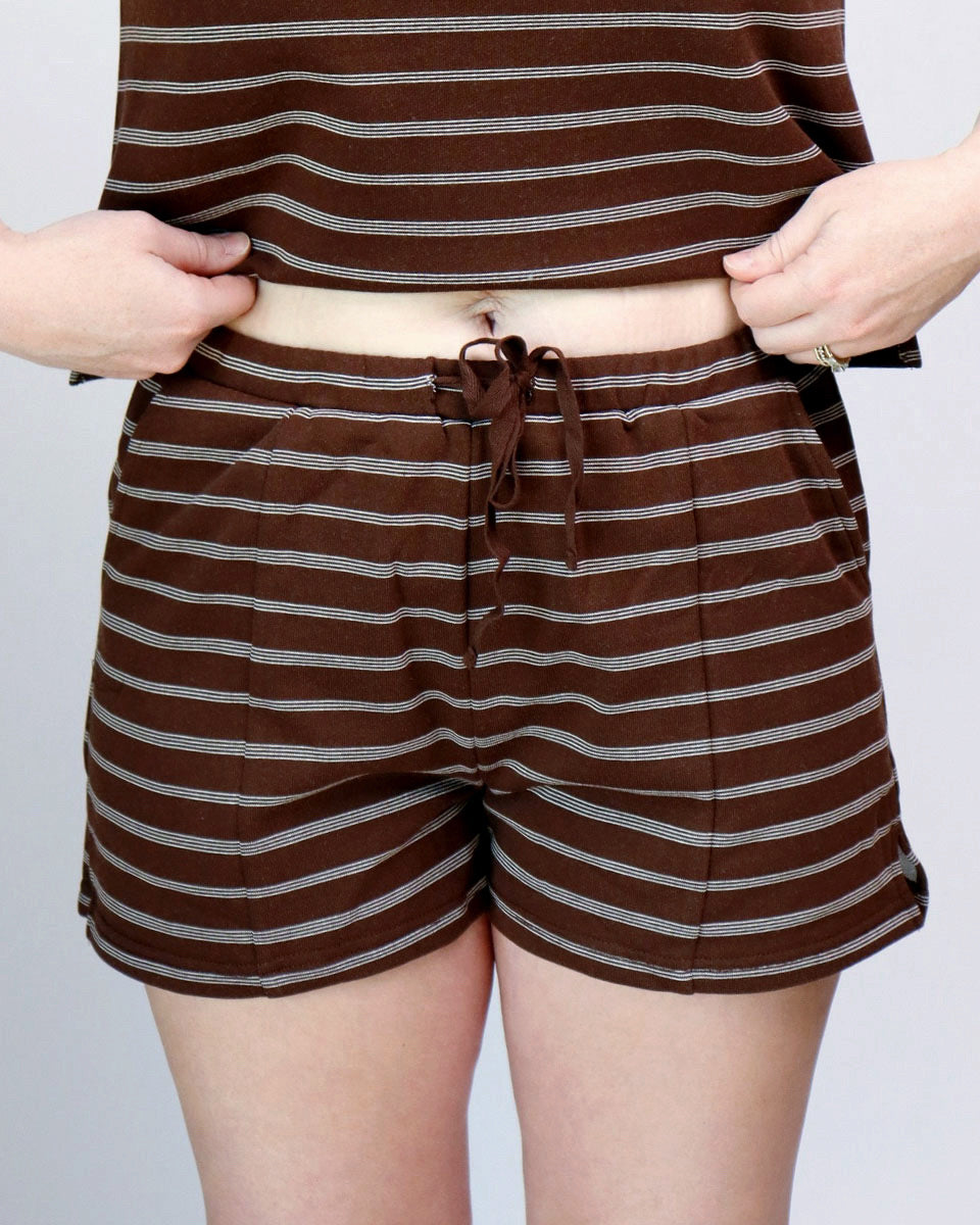 A person wearing brown and gray horizontally striped shorts with a drawstring waist, shown from the torso down against a light gray background.