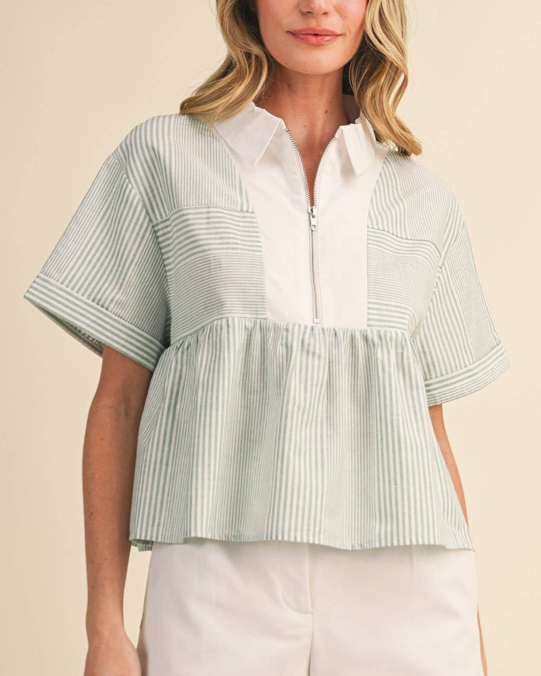 Woman wearing a light green and white striped shirt with white shorts on a beige background