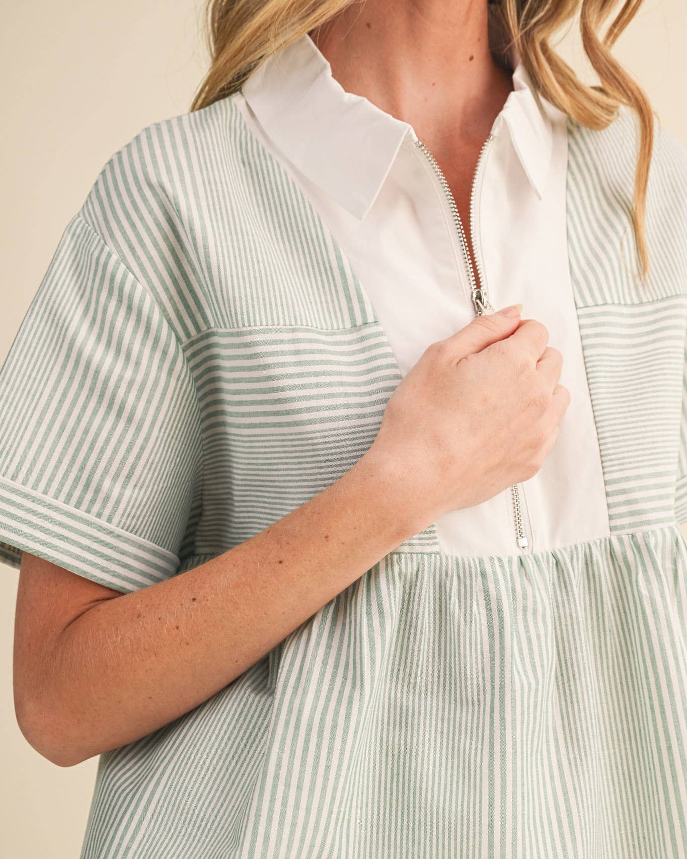 Woman wearing a light green and white striped dress over a white shirt.
