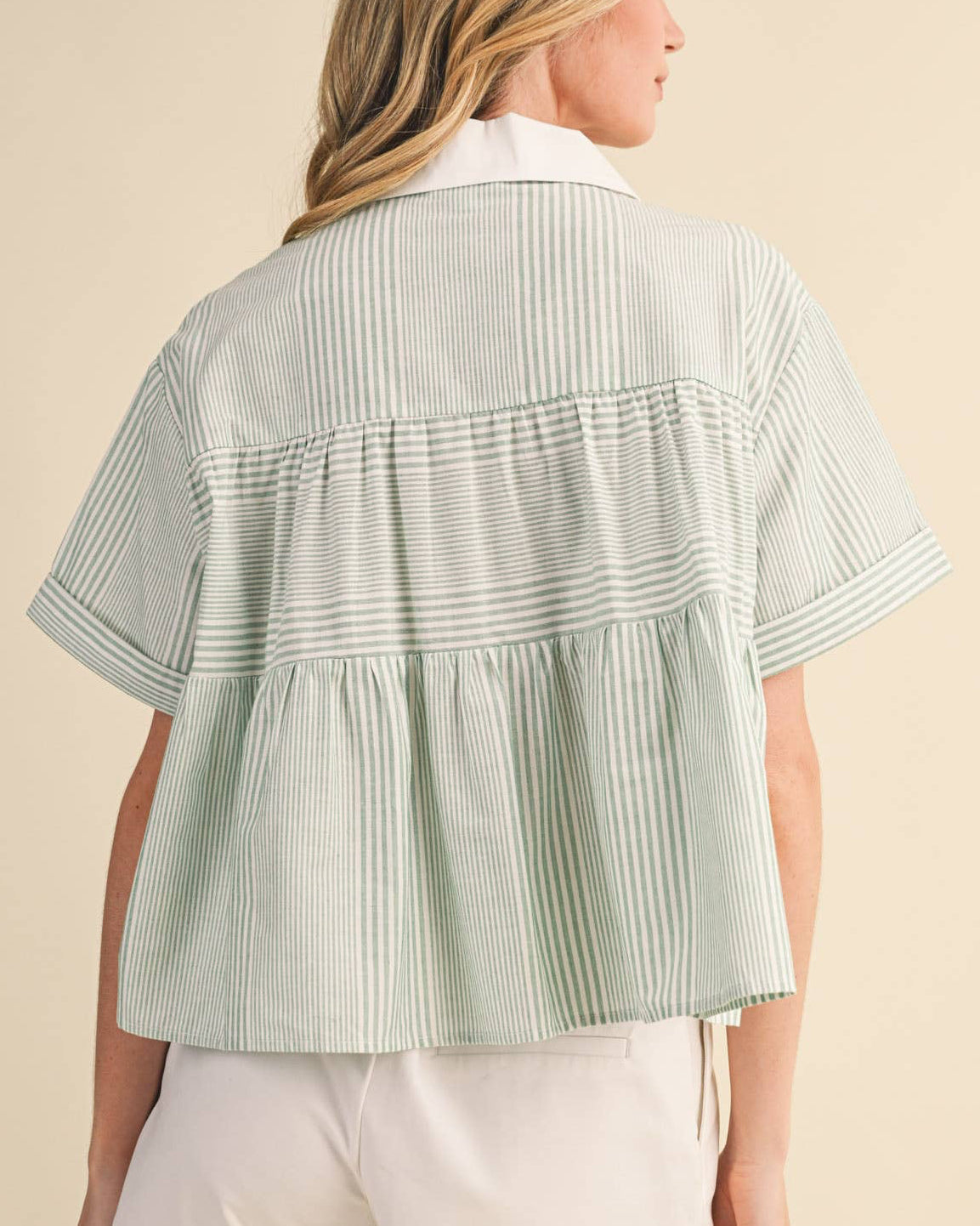 Woman wearing a light green striped shirt and white shorts on a beige background