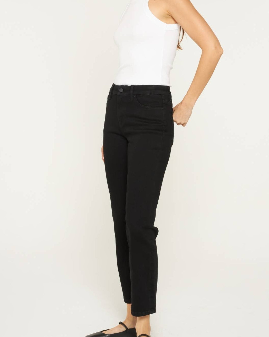 Model wearing black ankle length denim. Mid rise. on a neutral background. side view