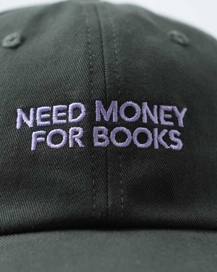 Black cap with 'NEED MONEY FOR BOOKS' text in purple on a white background