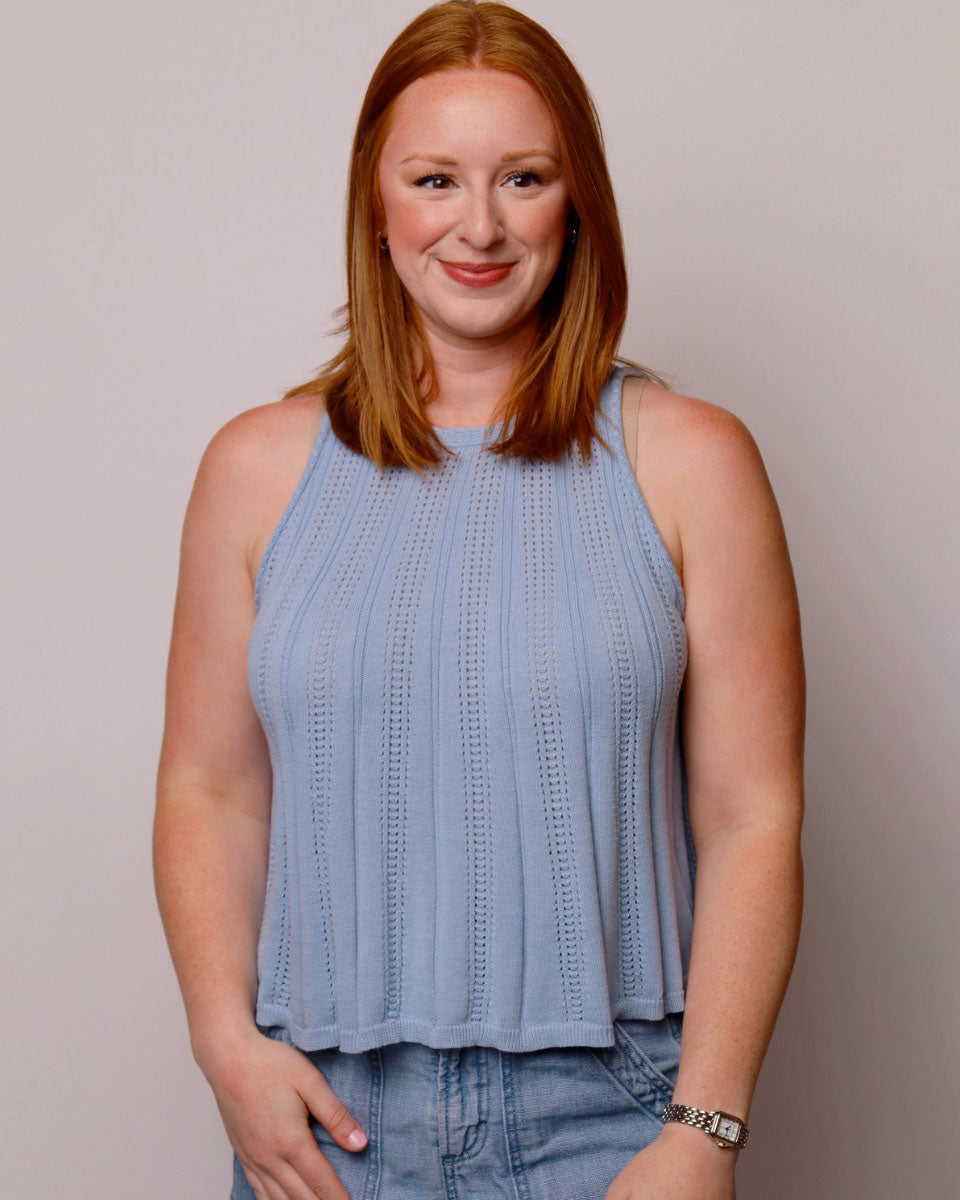 Woman wearing a light blue sleeveless top and jeans against a plain background