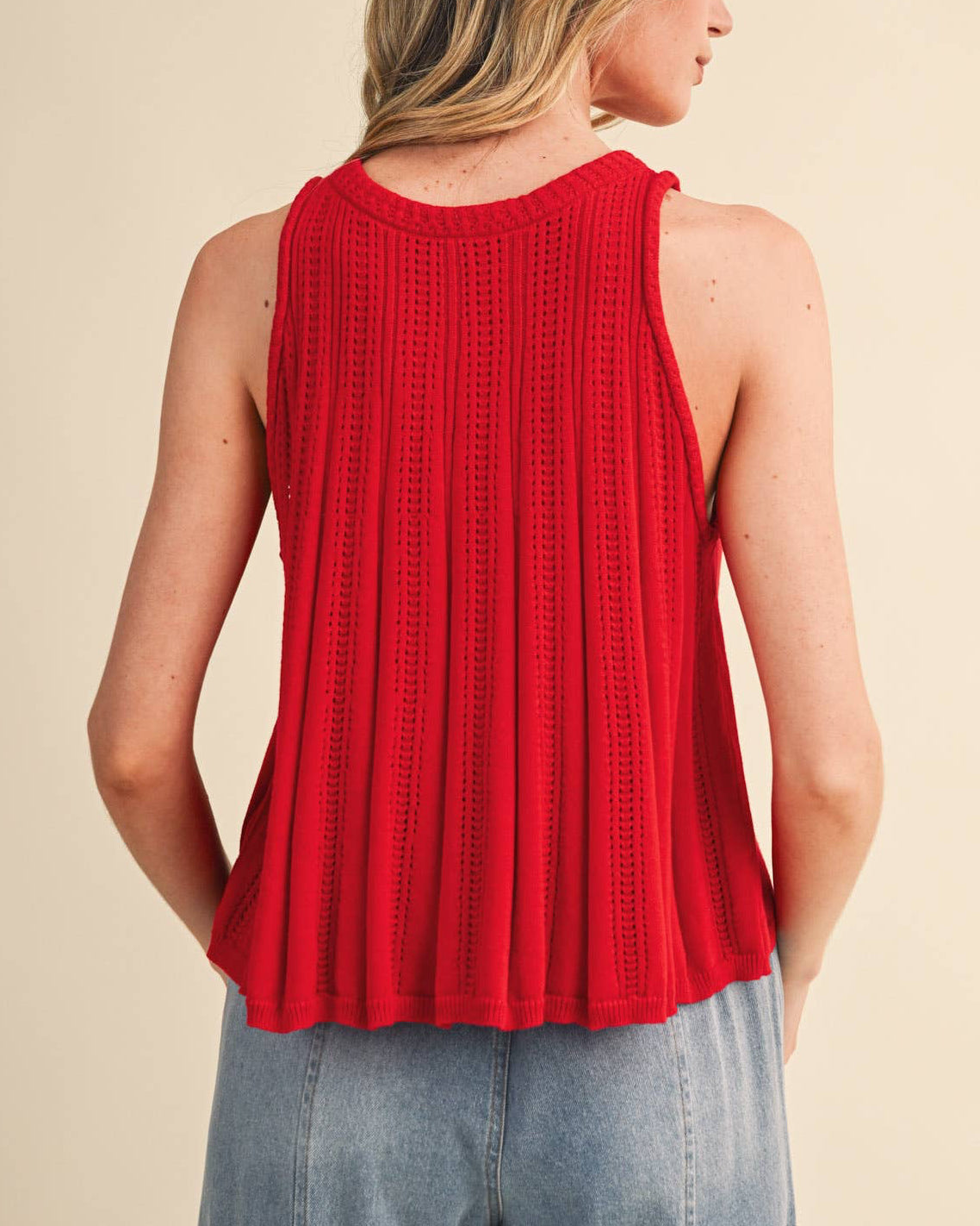 Woman wearing a red sleeveless top and light blue jeans on a beige background