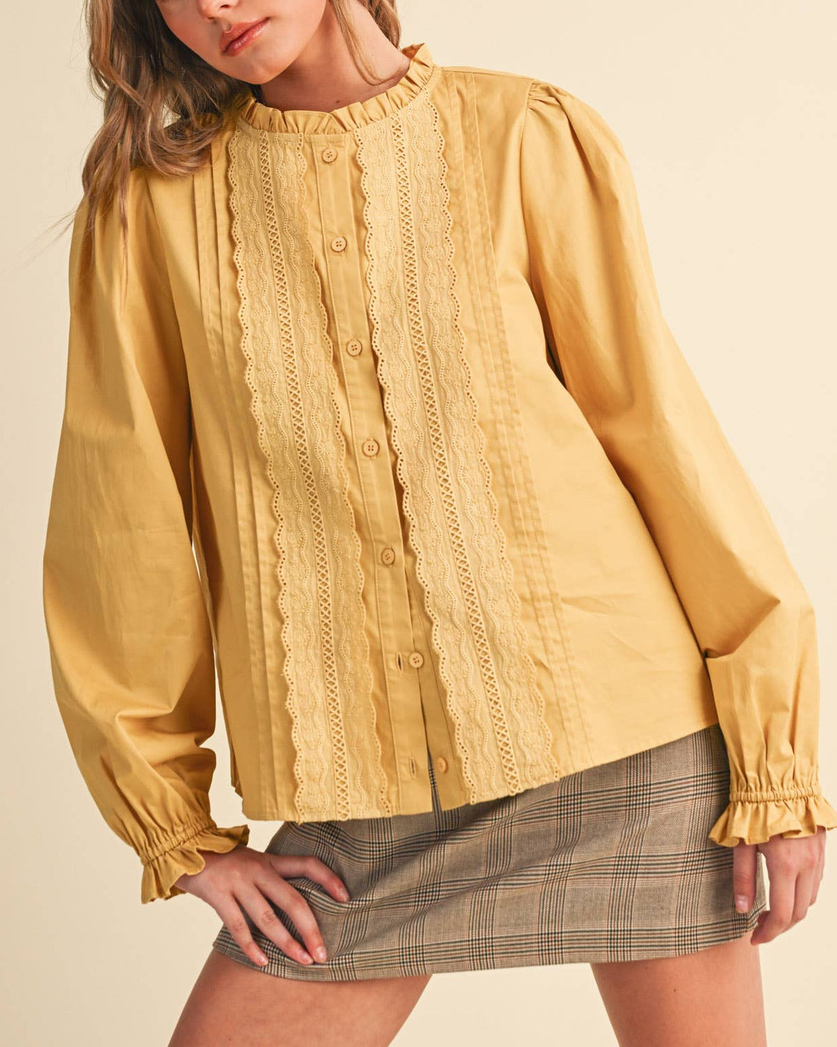 A woman wearing a honey gold long sleeve button up blouse with lace details on a neutral background