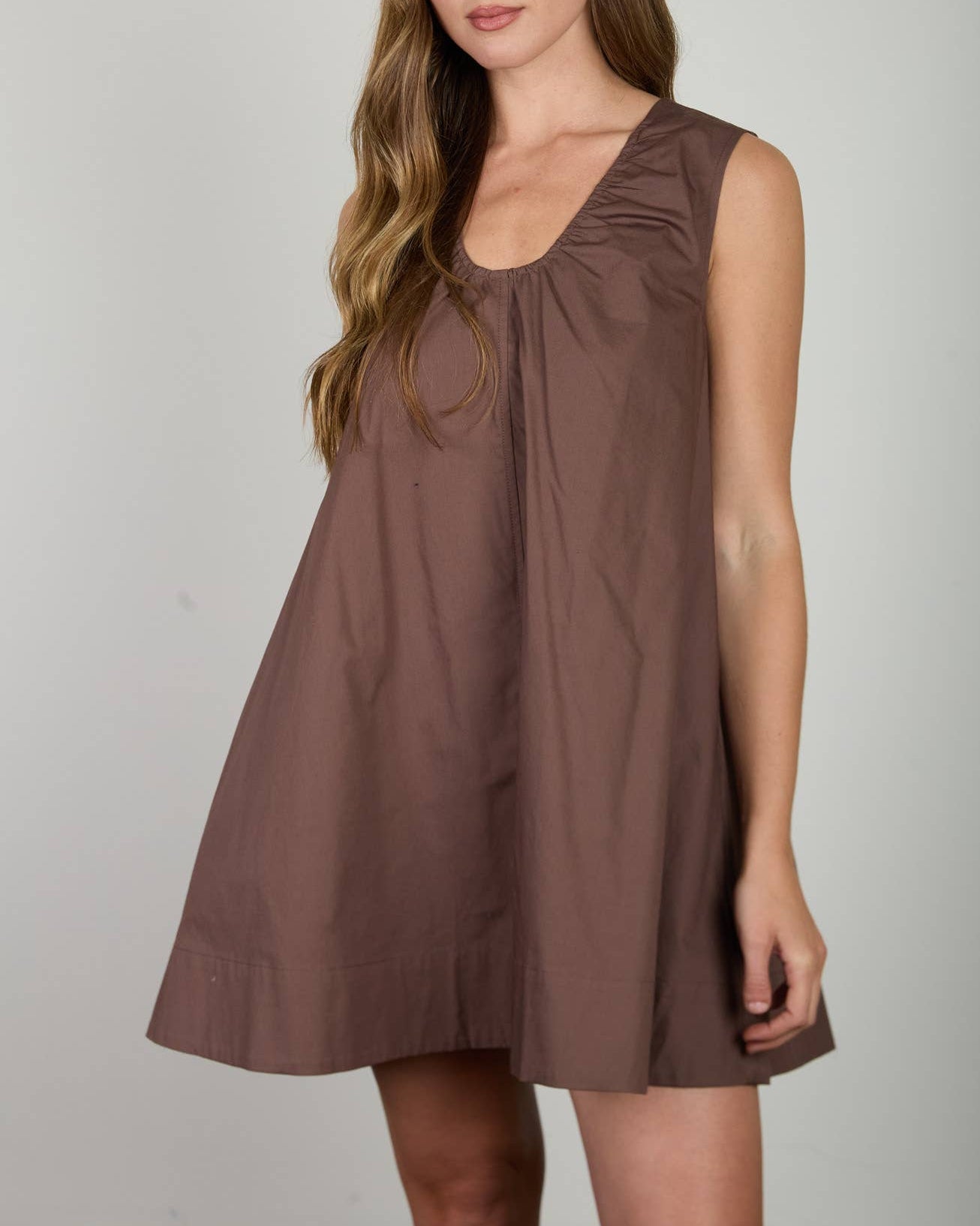 Model wearing a brown sleeveless dress against a neutral background