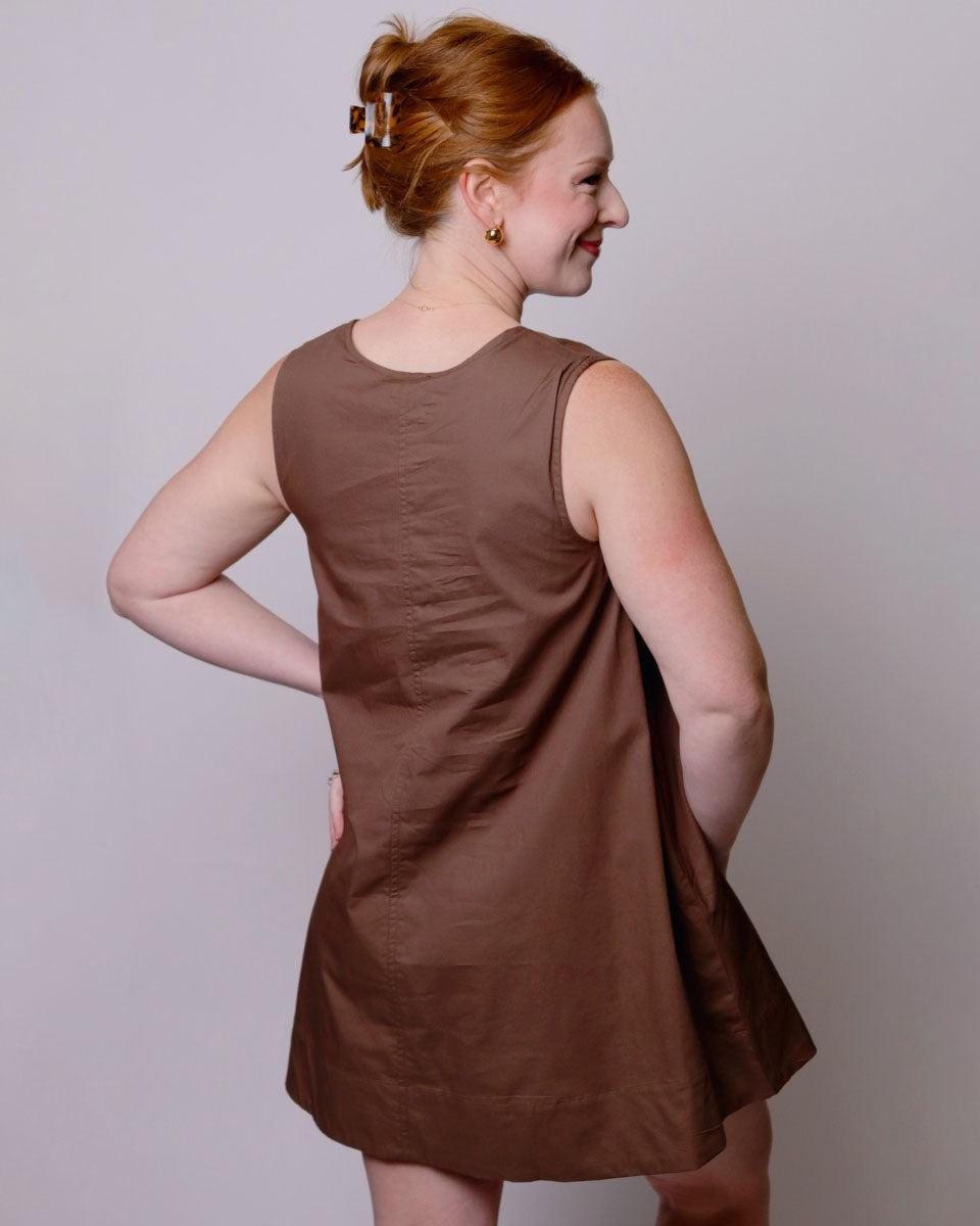 Woman wearing a brown sleeveless dress against a plain background