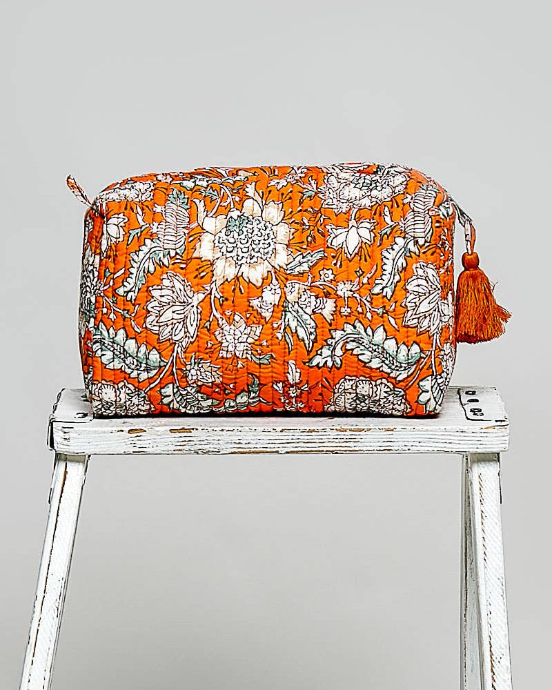Floral patterned bag with orange background on a white wooden stool against a gray background