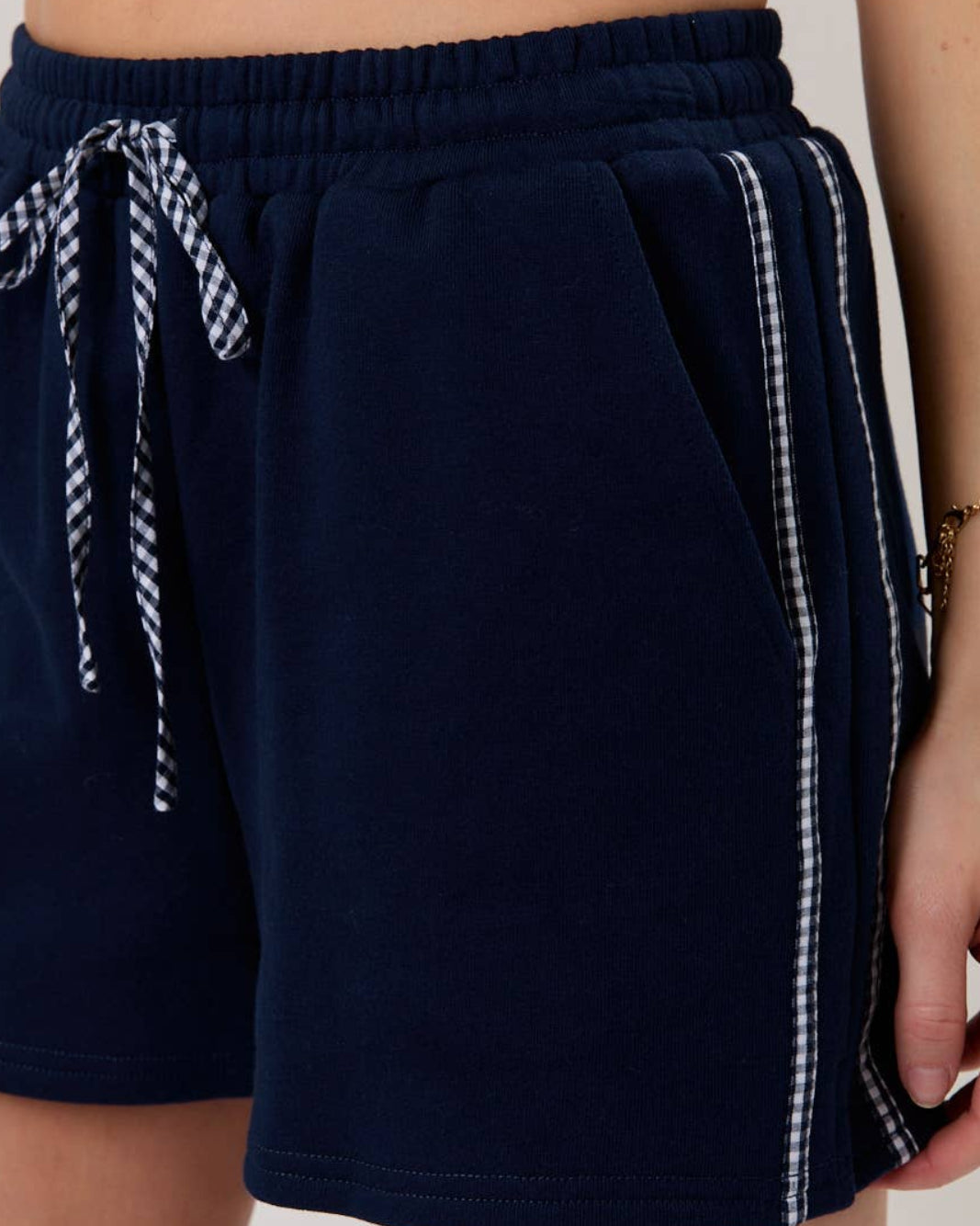 model wearing a navy blue pair of shorts with gingham contrast. neutral background. closeup view
