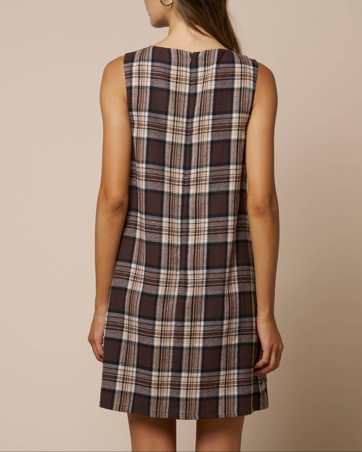 Model weaing a brown/taupe plaid sleeveless mini dress with diamond flower details on a neutral background back view