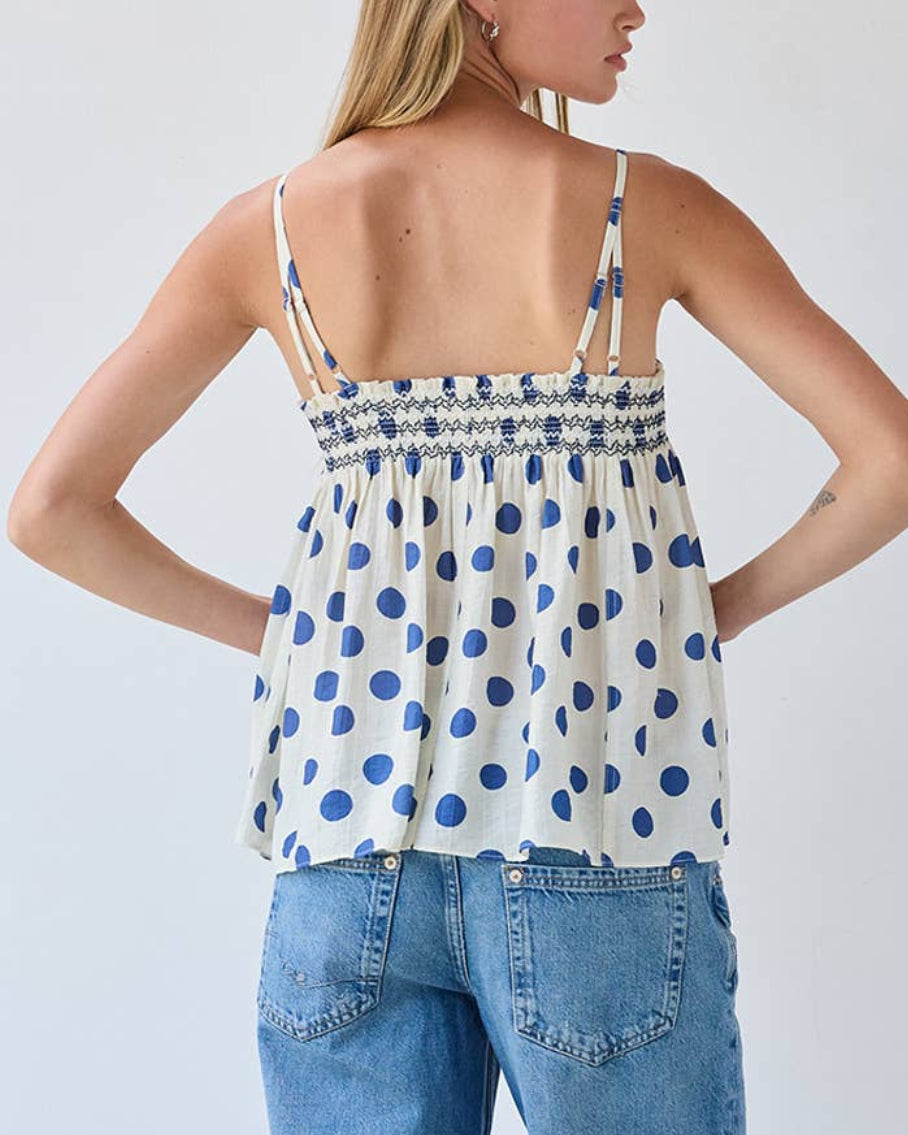 Model wearing a white tank top with blue polka dots on a neutral background back view