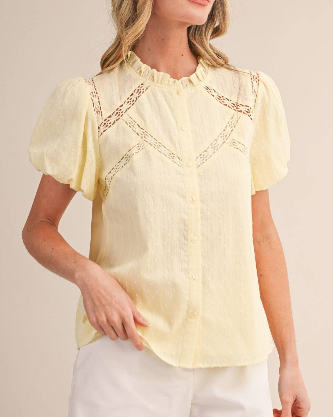 Woman wearing a yellow blouse with lace details and white shorts on a beige background
