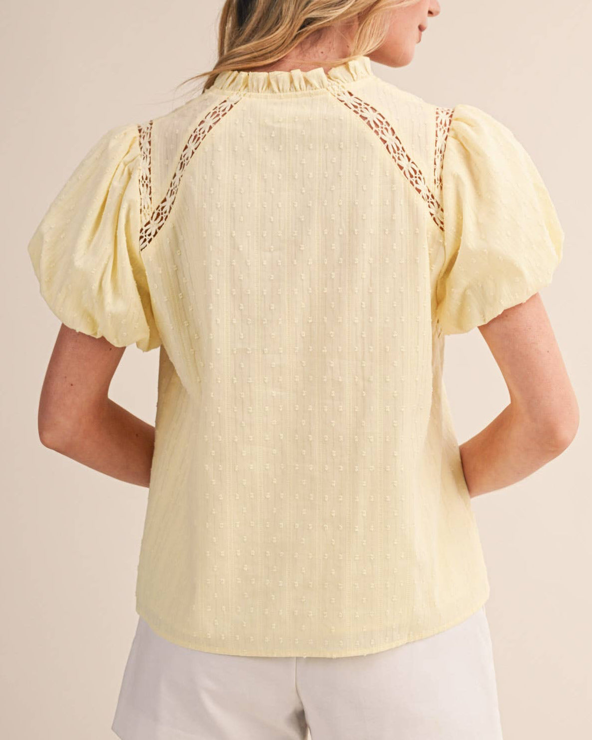 Woman wearing a yellow blouse with lace details on a beige background