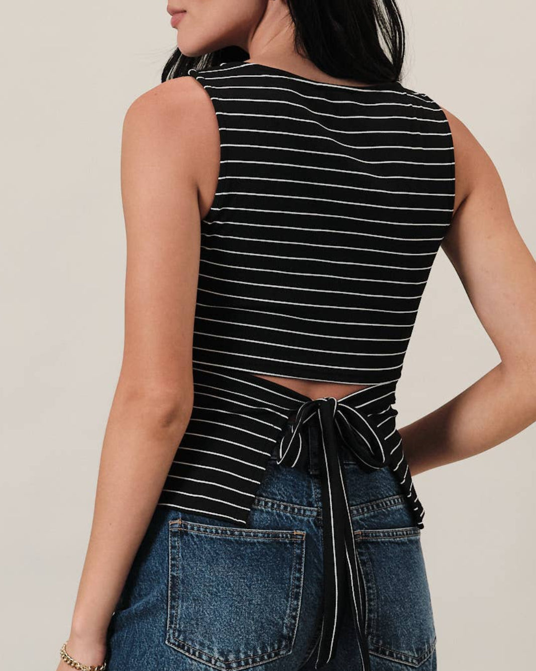 Model wearing a black and white striped tank top with ruching on the sides on a neutral background showing back detail