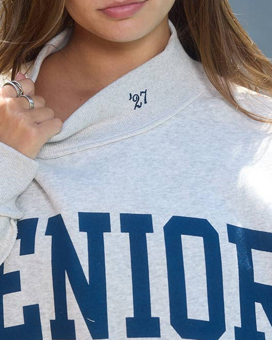 Person wearing a gray hoodie with 'SENIOR' printed in blue letters, standing outdoors.