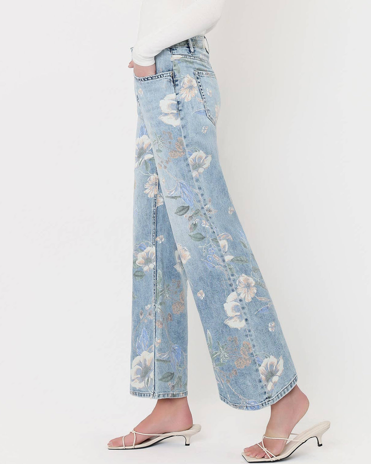 Woman wearing a white top and light blue floral jeans on a white background