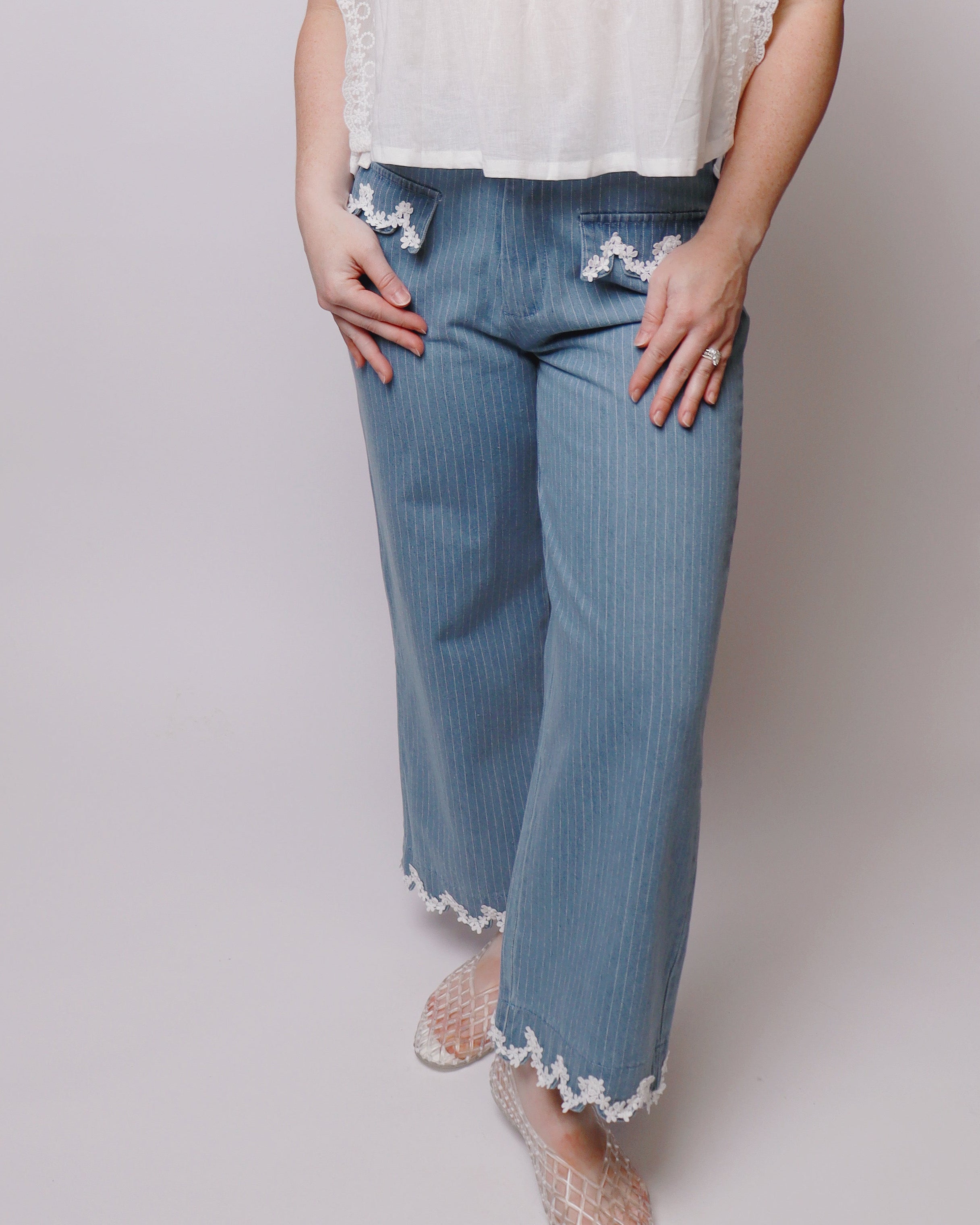 Woman wearing white blue pinch, striped jeans with floral embroidery around him and pockets standing in front of a white background