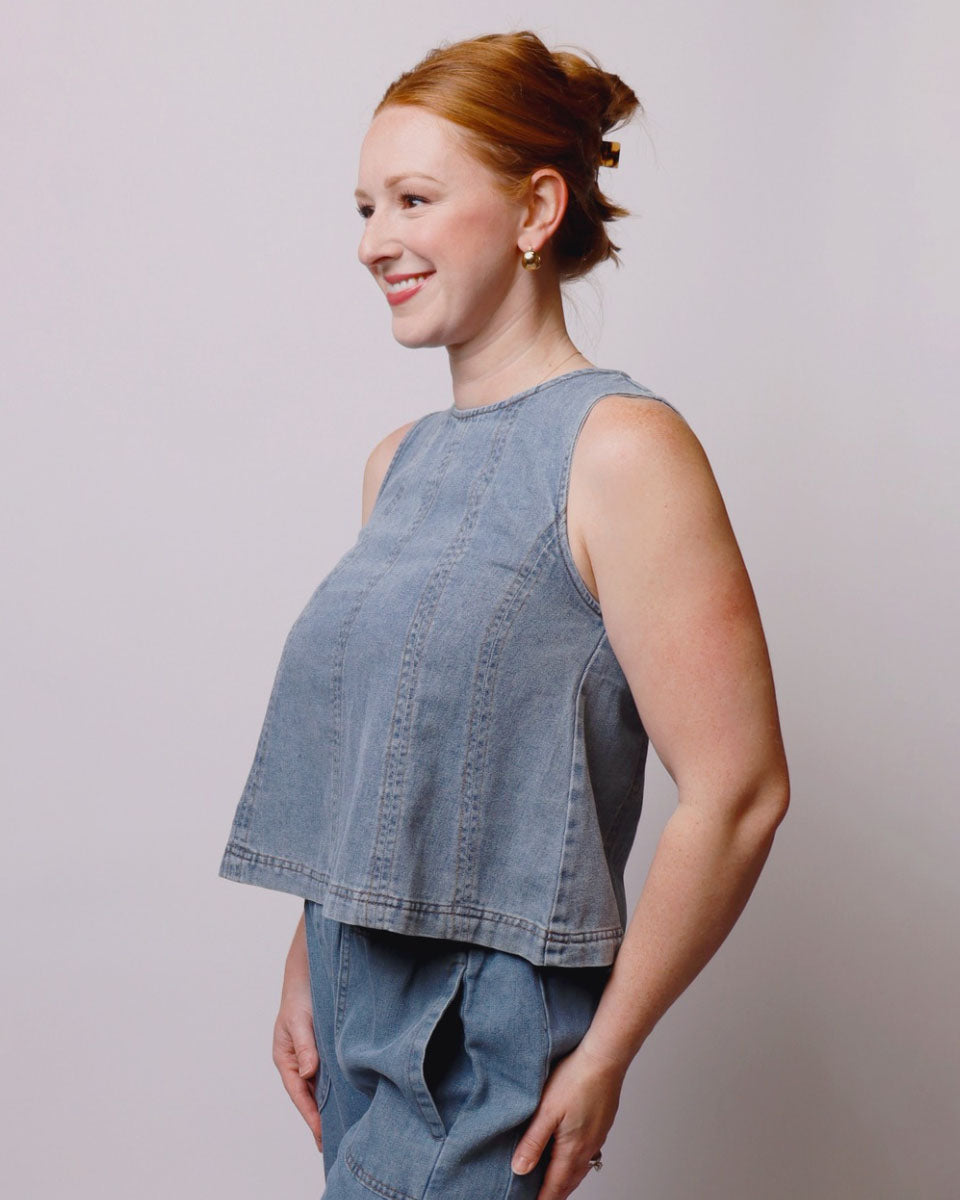 Woman wearing a denim sleeveless top and pants against a plain background