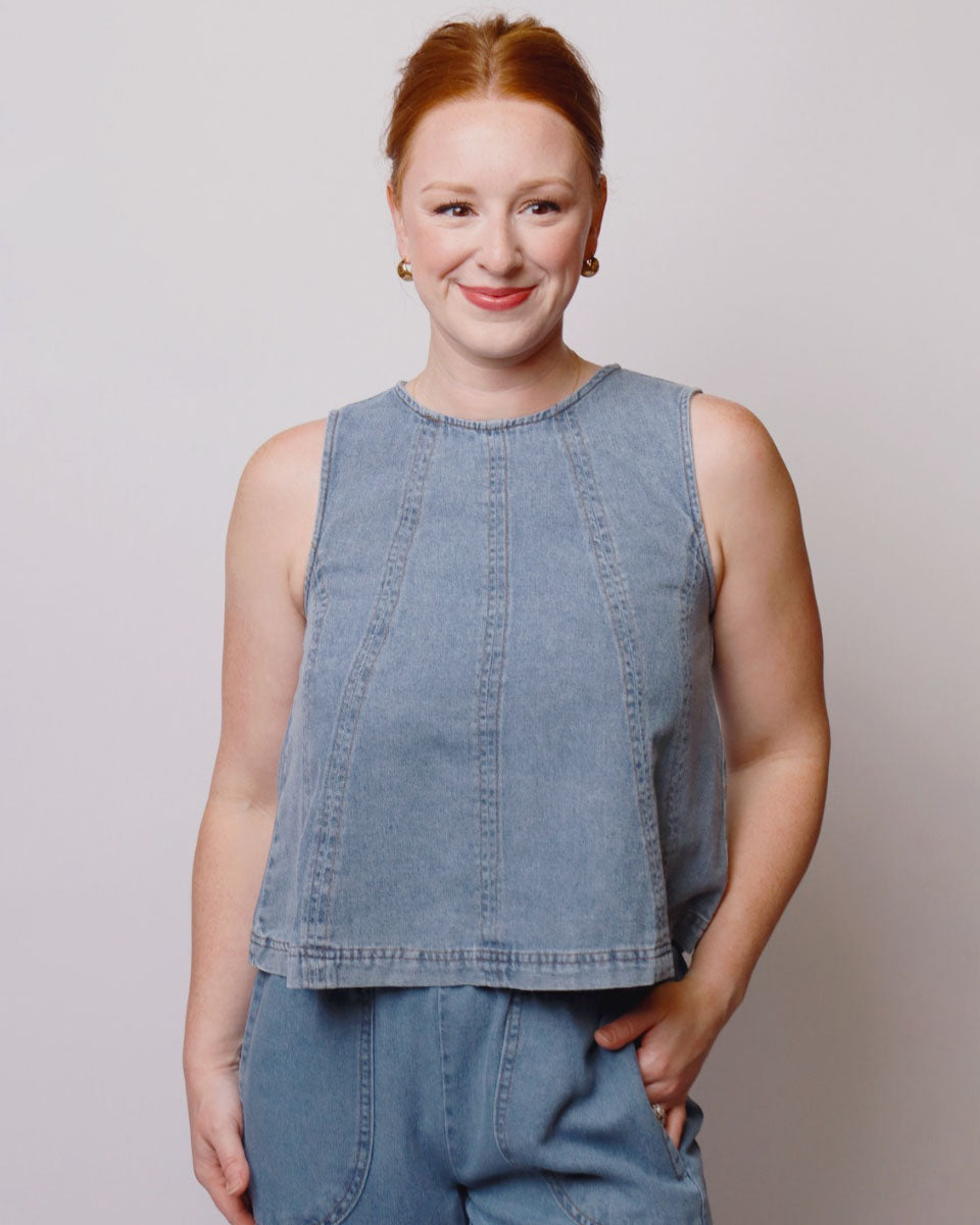 Woman wearing a sleeveless denim top against a plain background