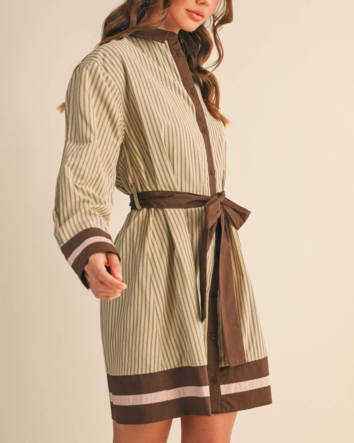 Model wearing a beige and brown striped belted mini dress on a neutral background.