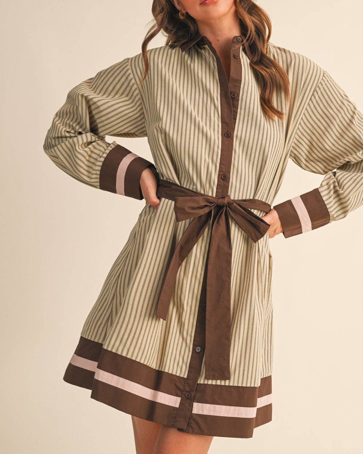 Model wearing a beige and brown striped belted mini dress on a neutral background.